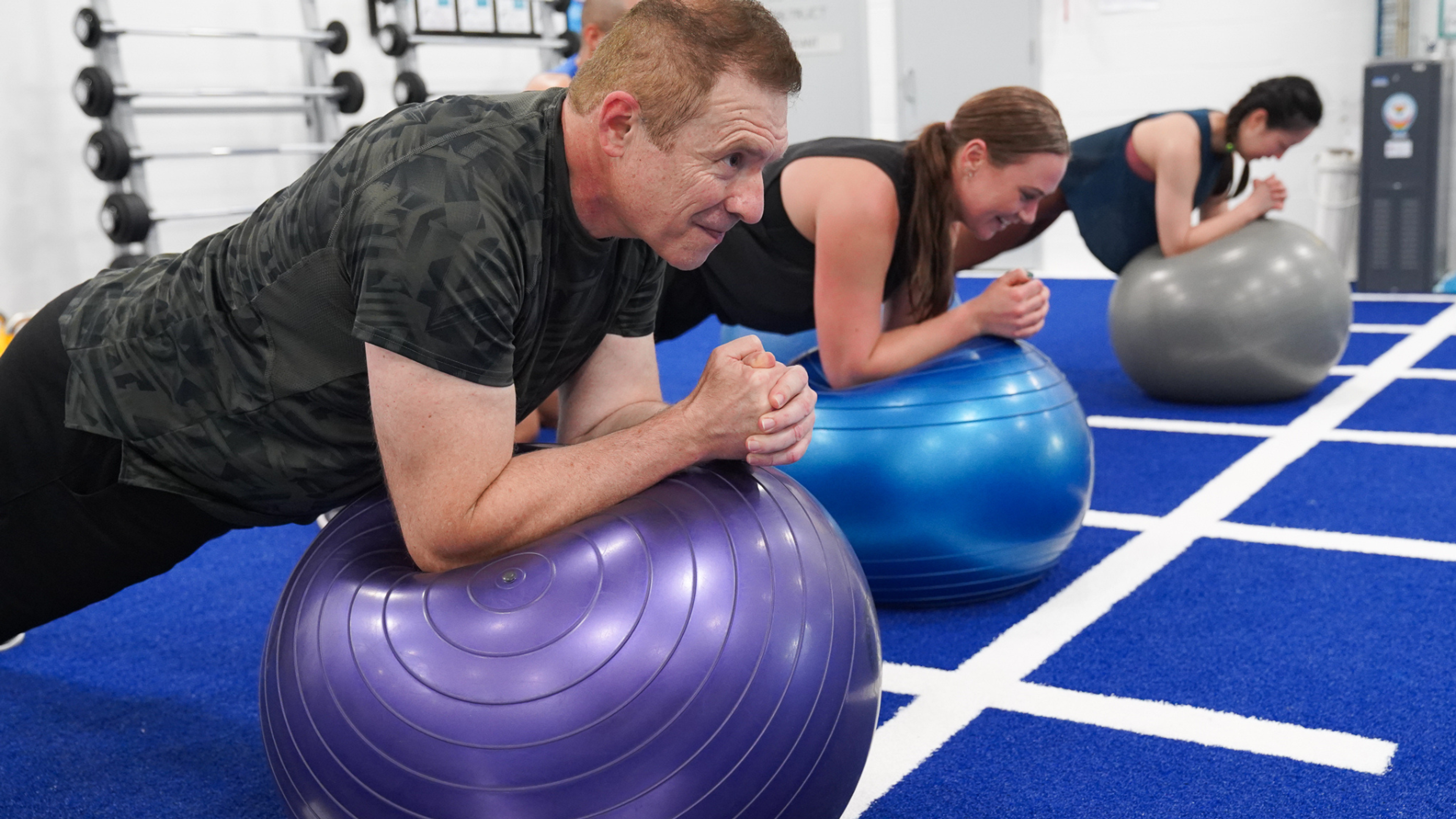 Three people planking on their forearms on top of large balls in the fitness studio at Cook + Phillip Park Pool