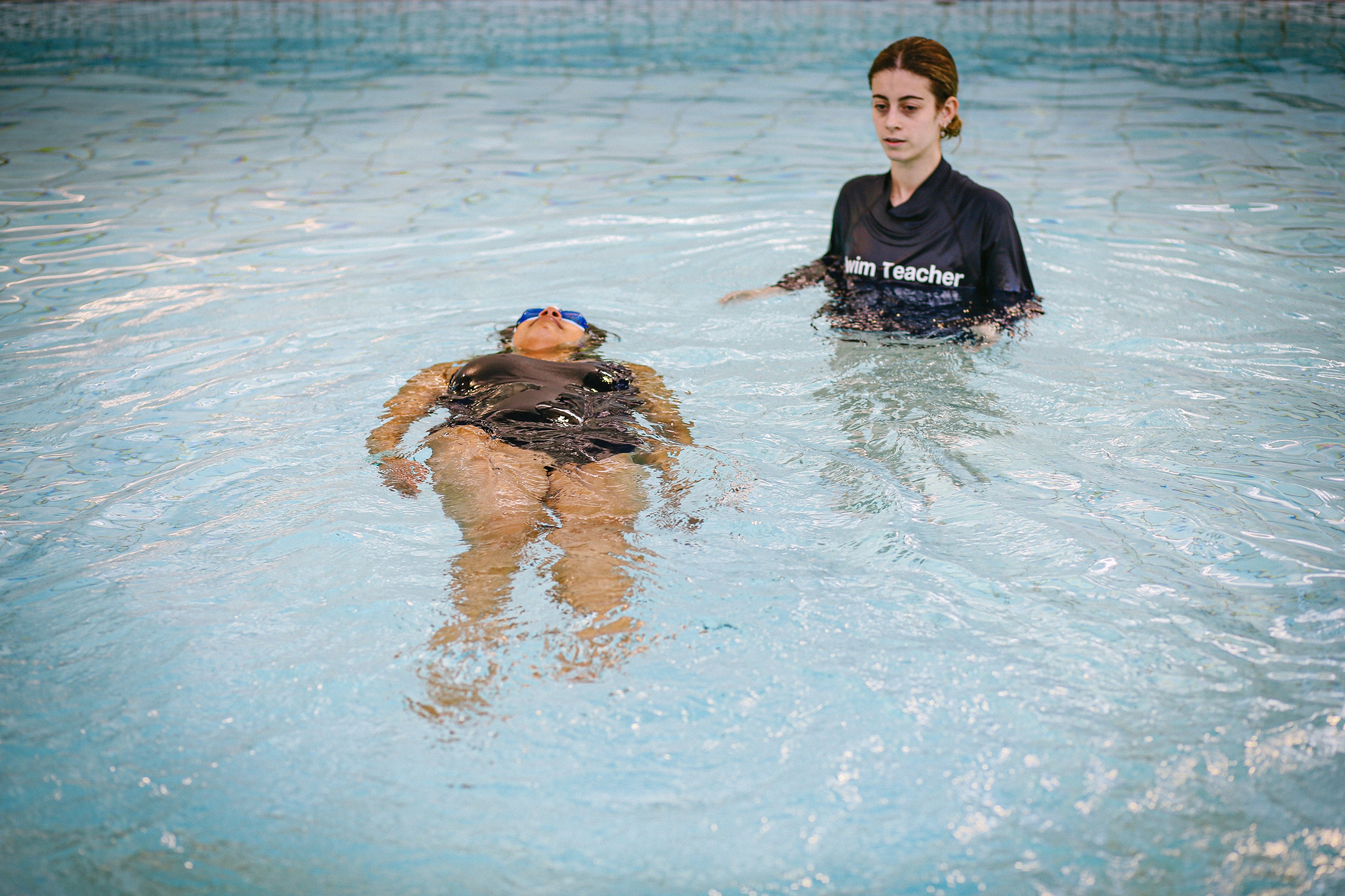 Swimming instructor watches an adult student float on their back in a swimming lesson