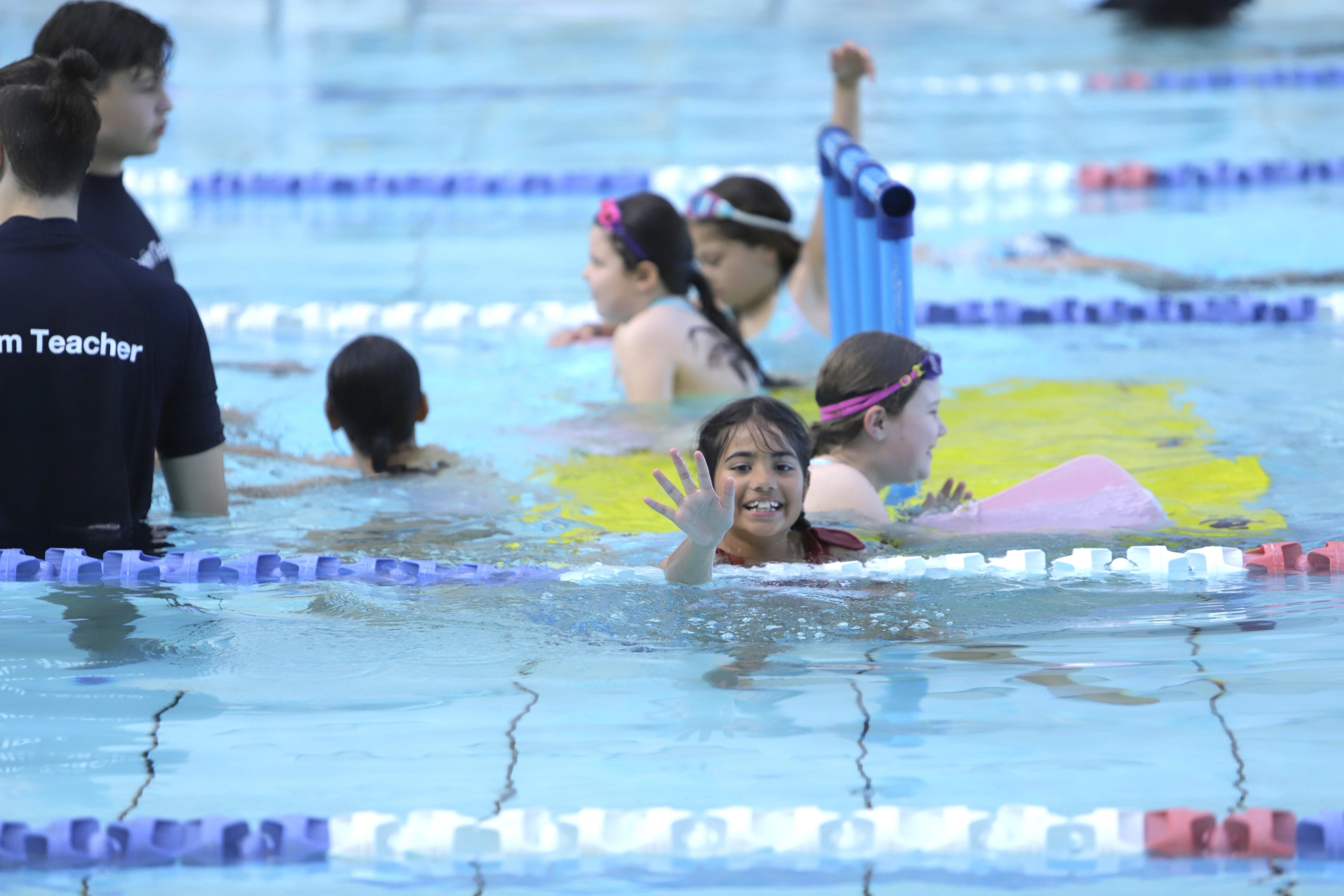 Young girl smiling and waving at the camera during a Learn to Swim class at Gunyama Park