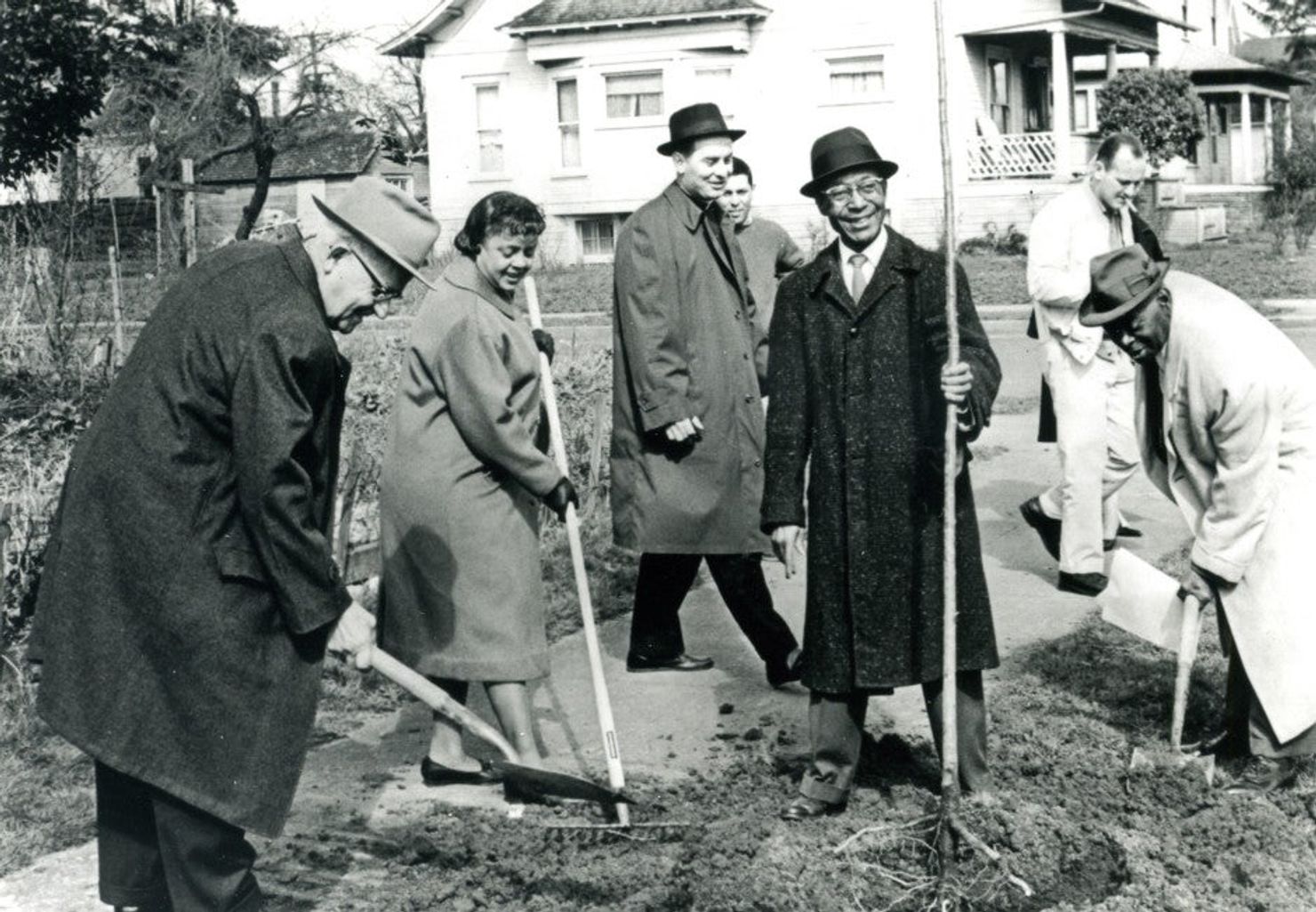 Several happy people in long coats digging with shovels.