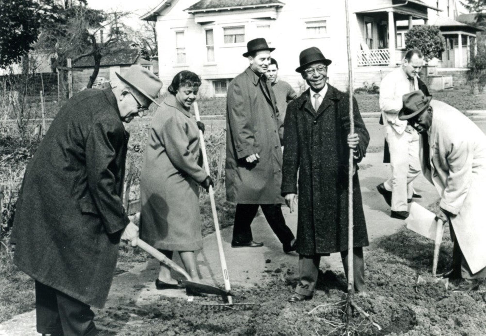 Several happy people in long coats digging with shovels.