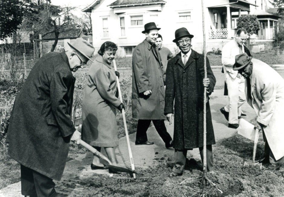 Several happy people in long coats digging with shovels.