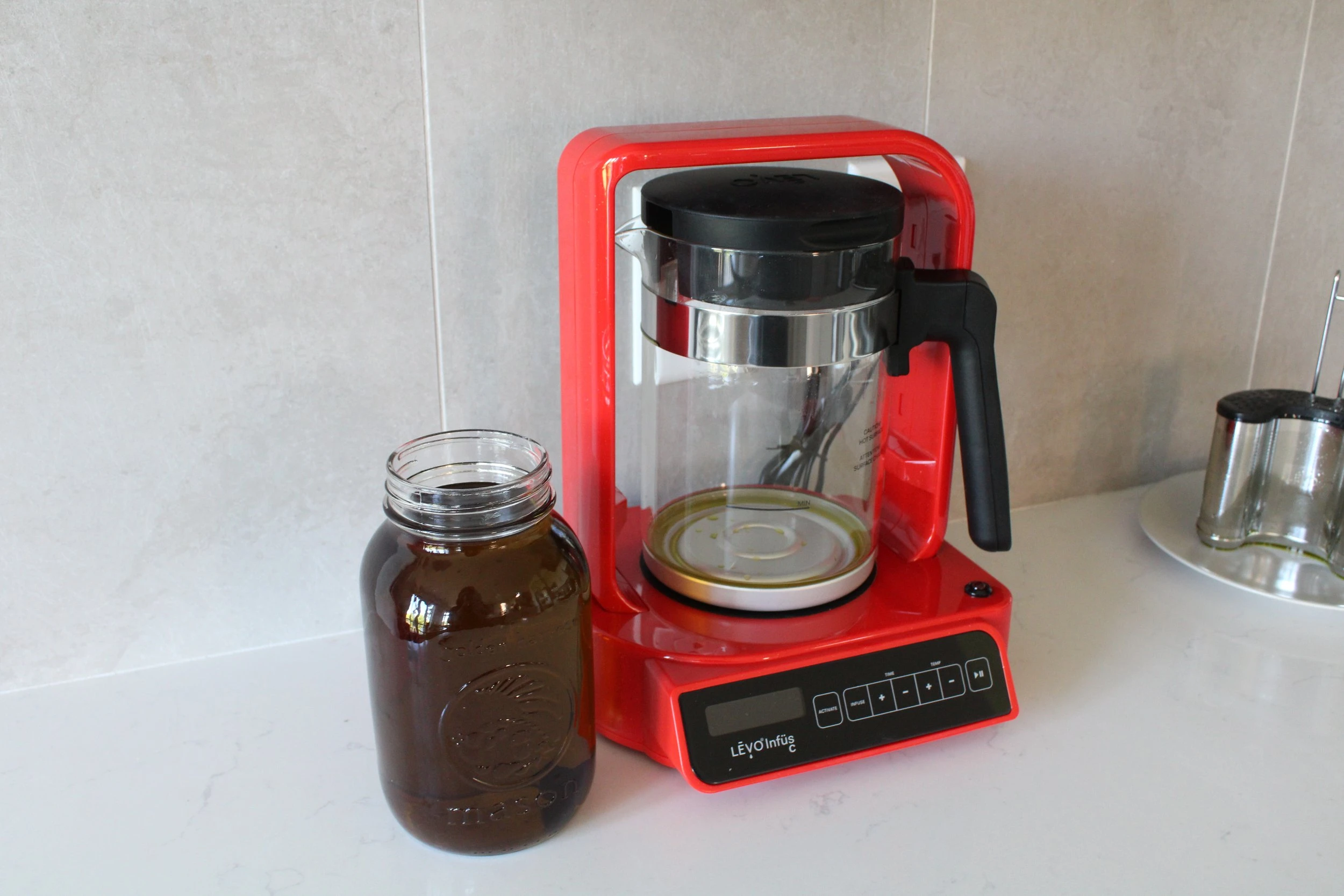 The red LEVO machine and a large mason jar of infused oil next to it on a white marble counter.