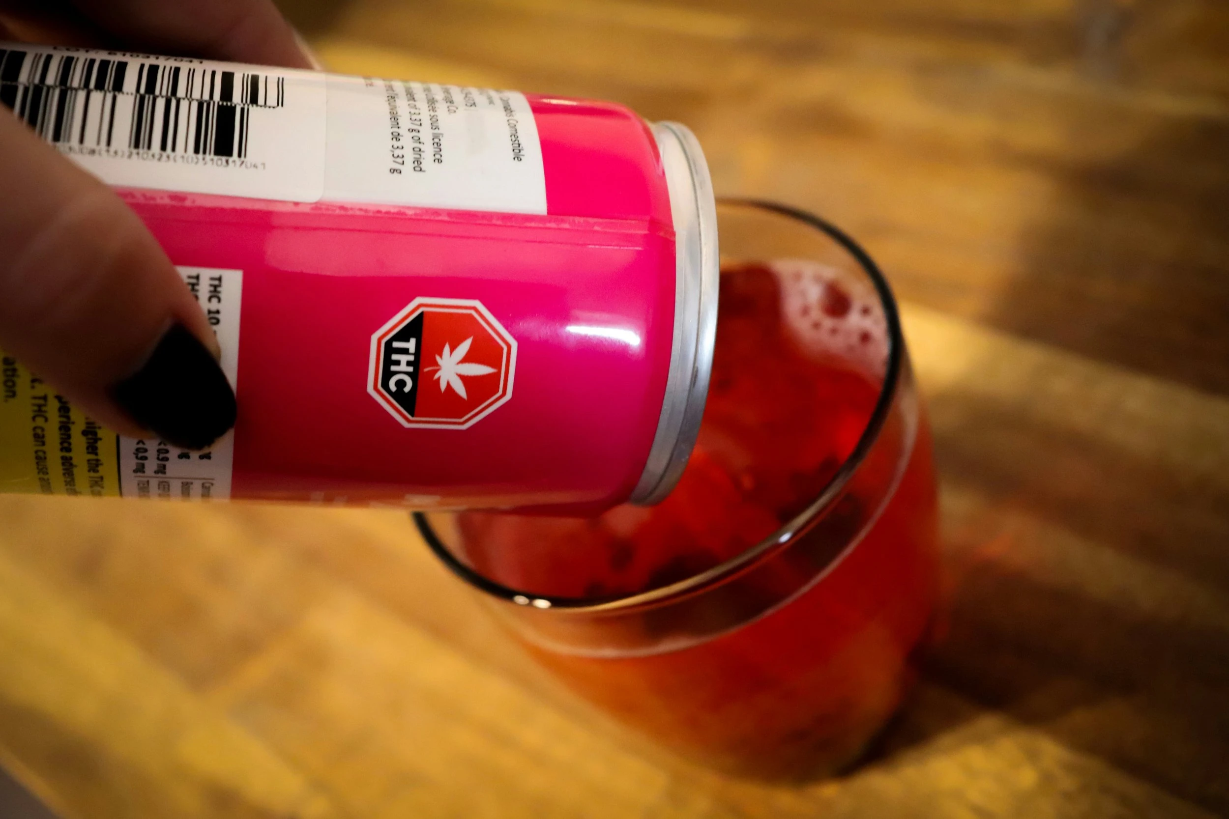 A pink cannabis beverage being poured into a small glass with ice.