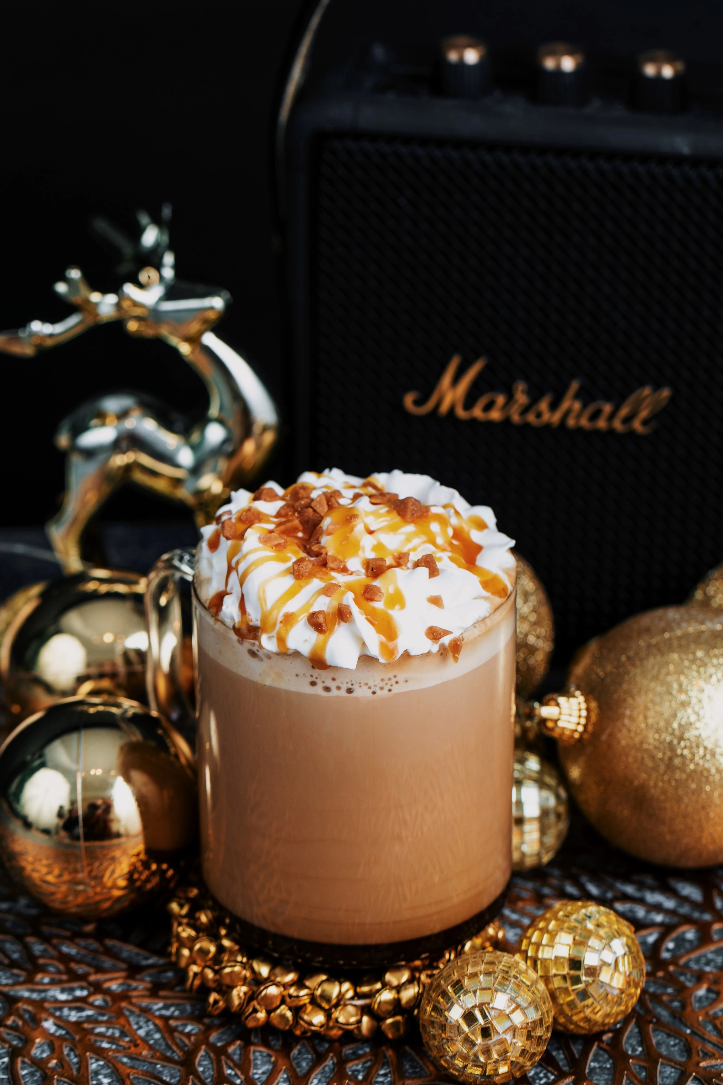 A glass mug holding a cannabis infused caramel brûlée latte topped with whipped cream and caramel sauce and resting on a knitted coaster.