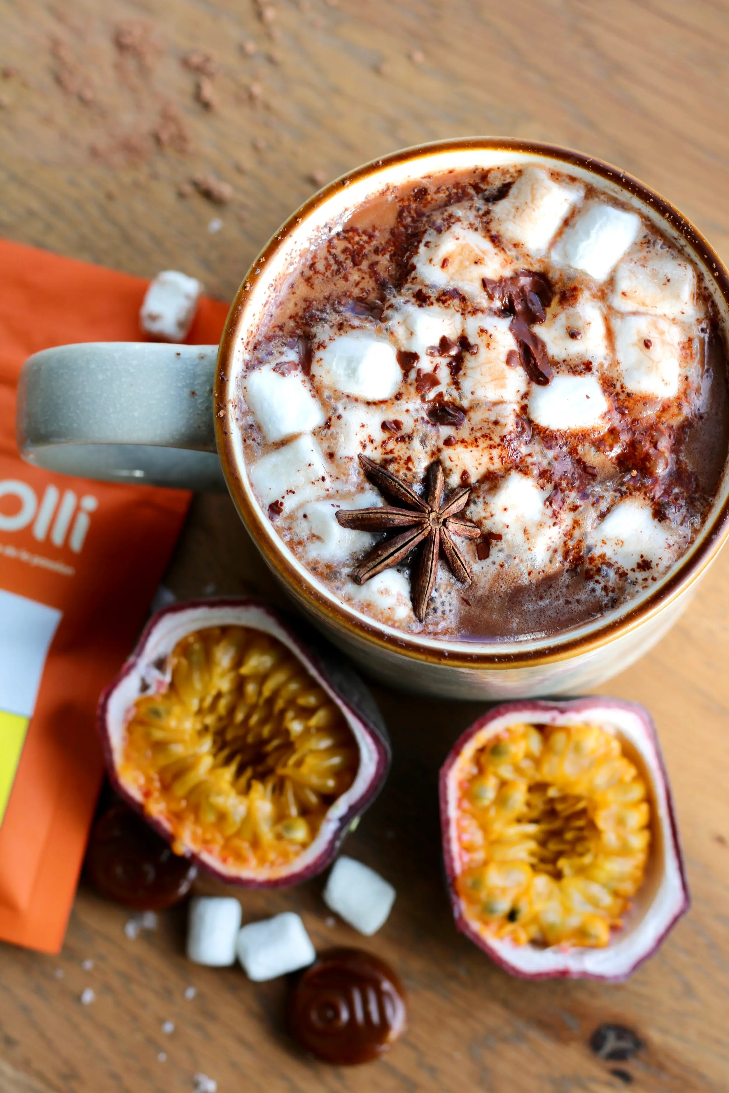 an aerial shot of a large mug of hot chocolate with mini marshmallows and a star anise garnish. Beside the mug are two halves of a passionfruit and some mini marshmallows.