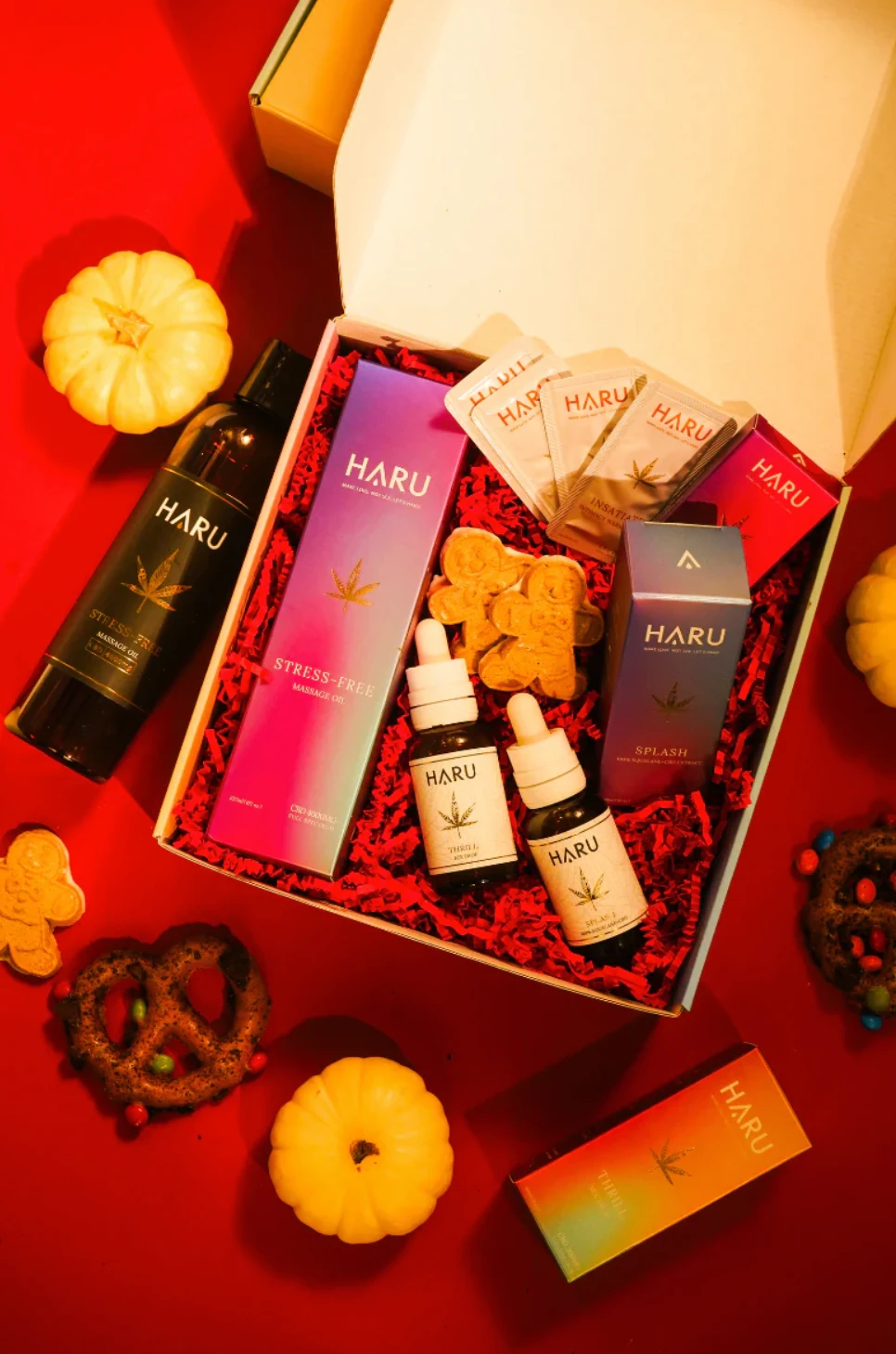 A bundle basket of infused oils sit in a box with red tissue paper as other festive snacks sit around it.