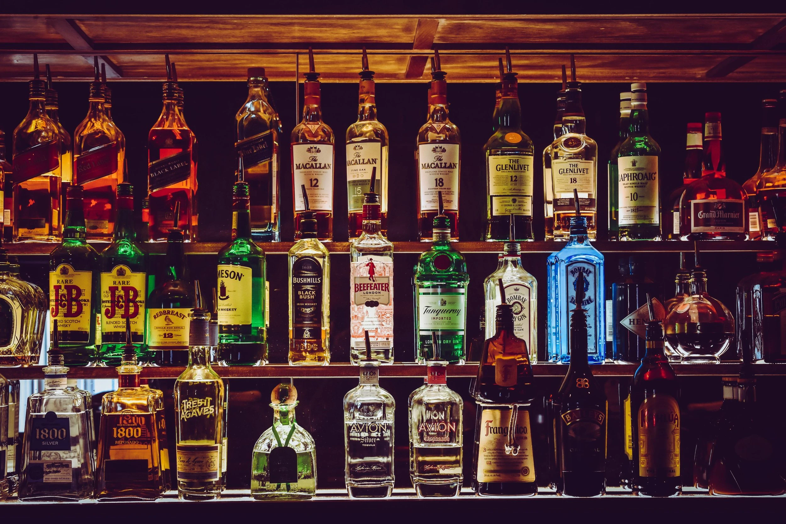 Three shelves of bar liquor/rail lined up in no particular order.