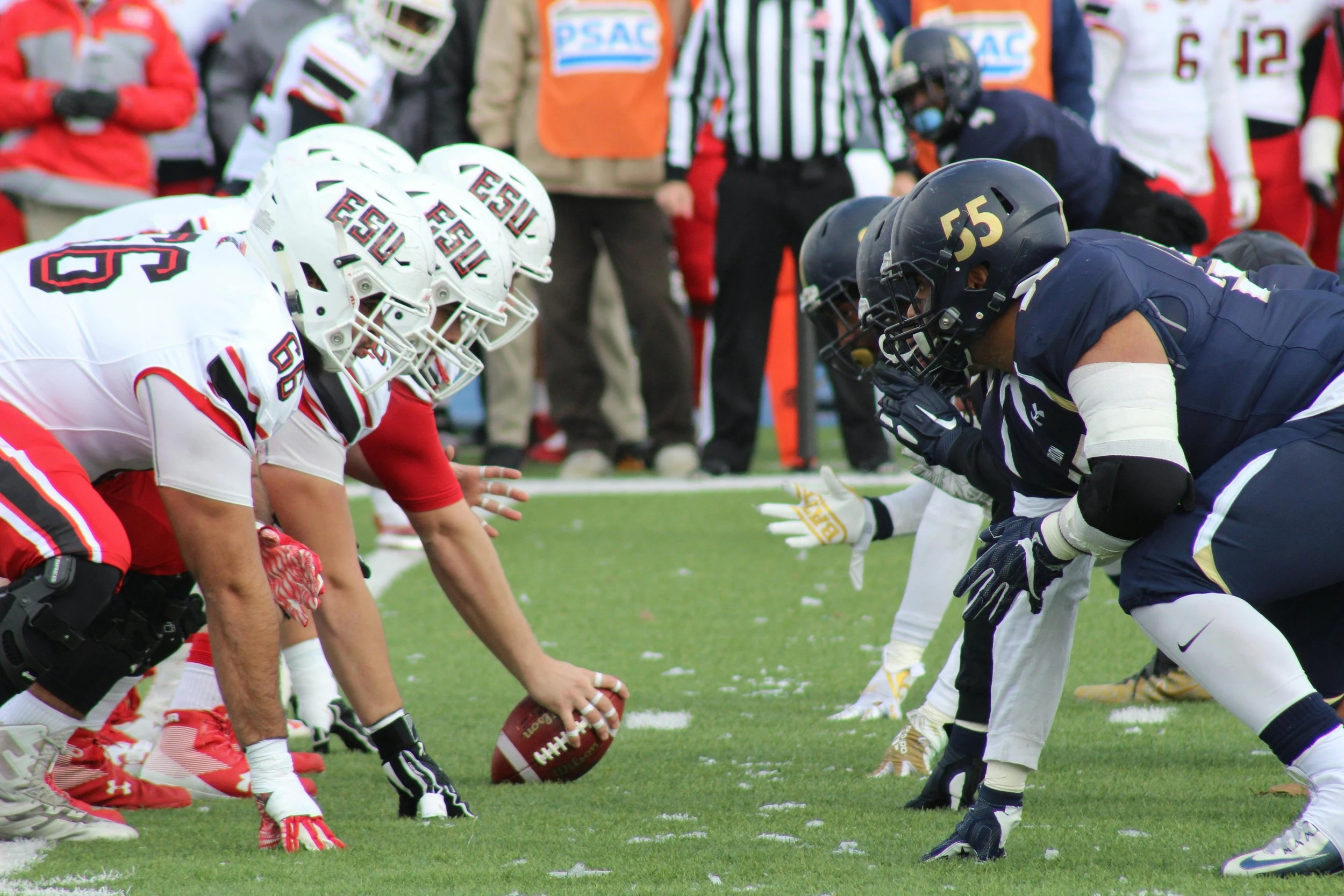 A starting lineup face-off of a football game, two different teams are crouched in a line staring at each other whilst waiting for the ref to start the game.