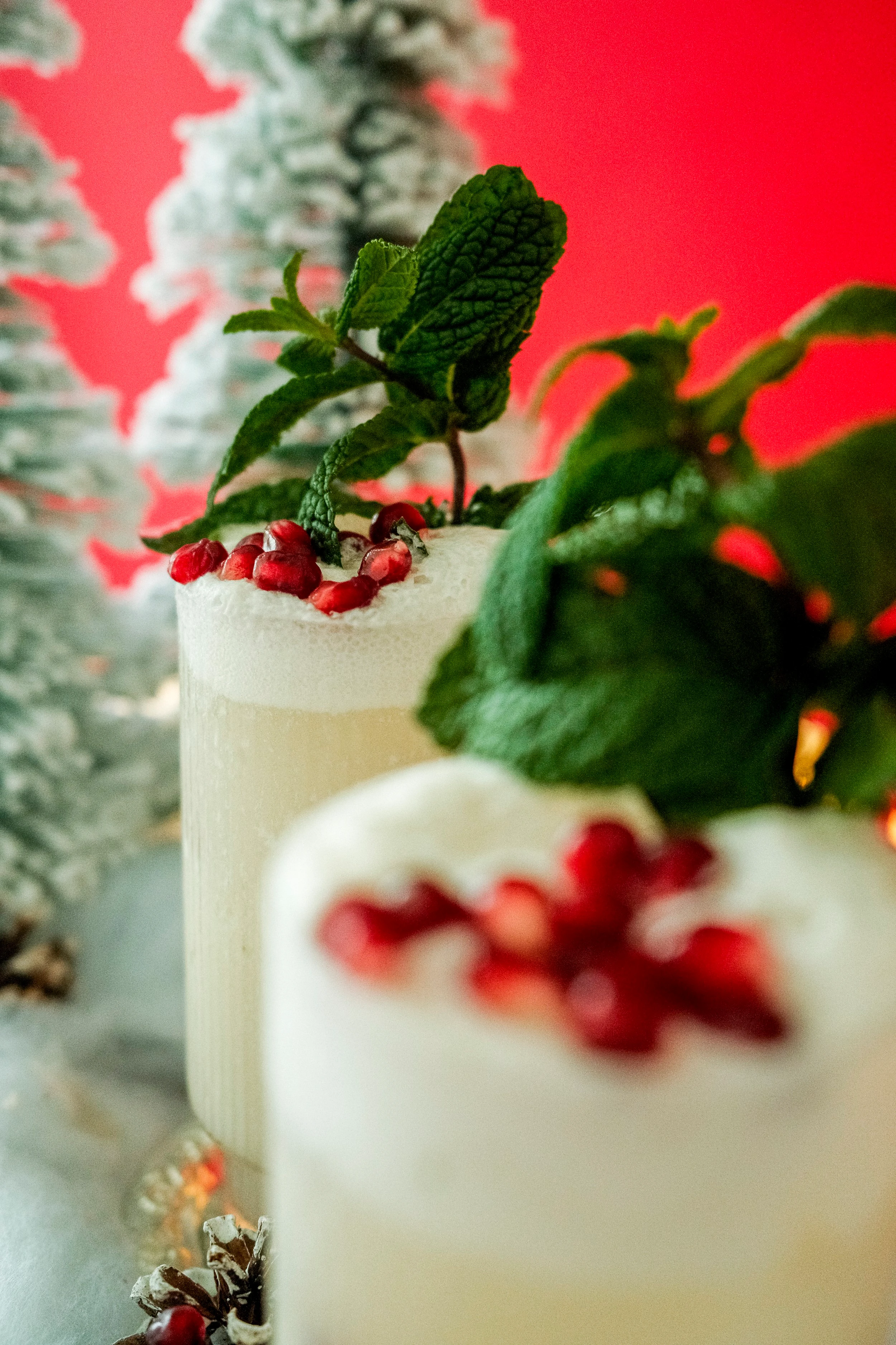 Two tall, clear glasses which hold a cannabis infused sparkling beverage and are topped with red pomegranate seeds and sprigs of mint.