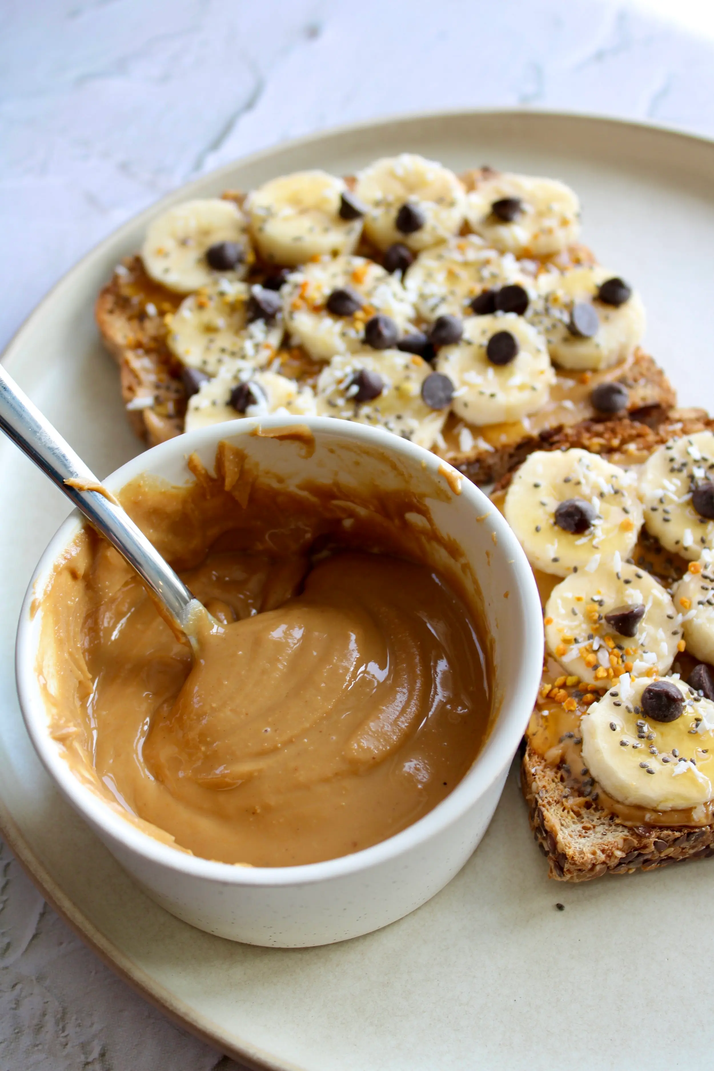 a large bowl of melty peanut butter with a spoon in it, along with two slices of peanut butter banana toast behind it. 