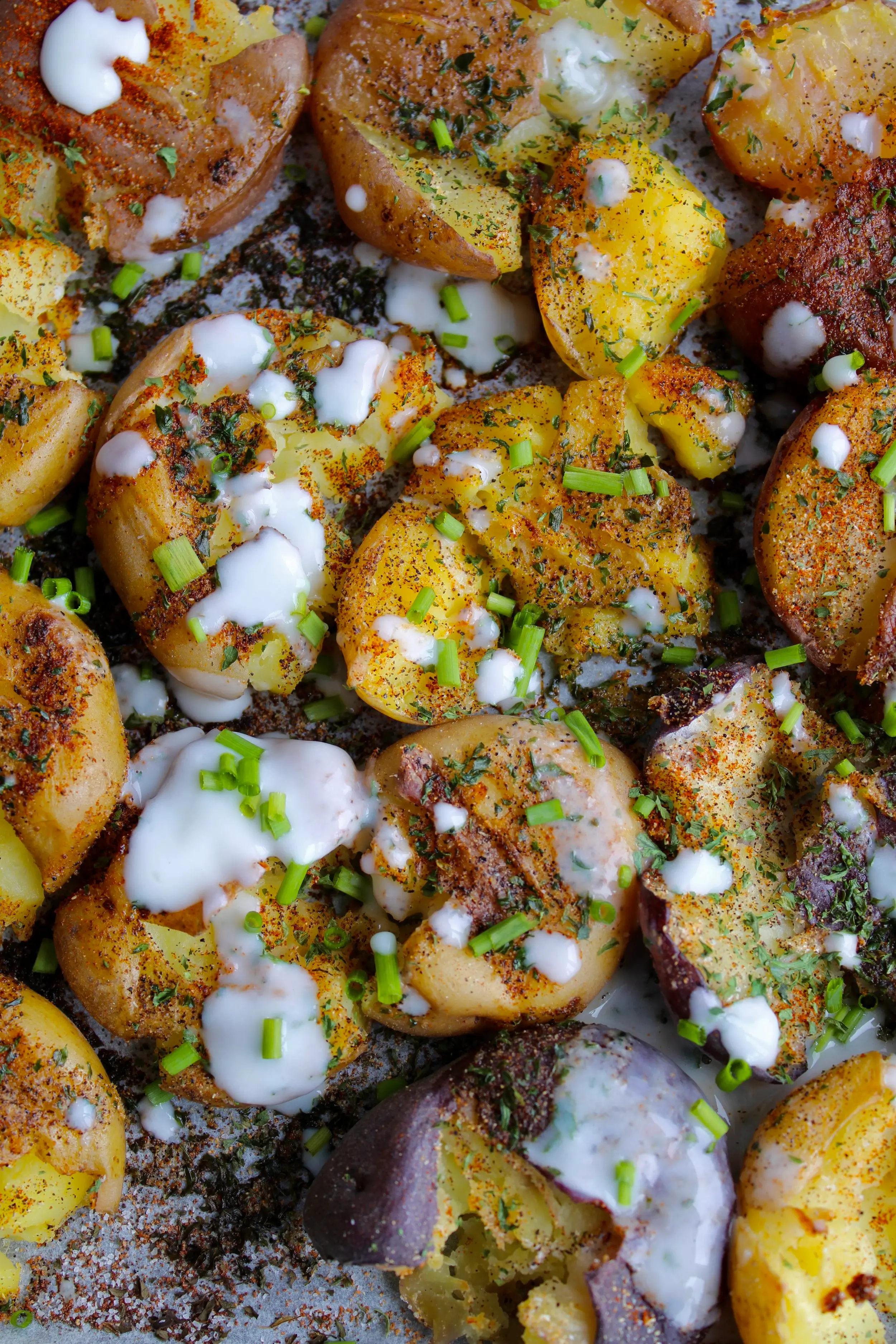 A close up shot of crispy potatoes with colourful seasoning and a cream drizzle on top.