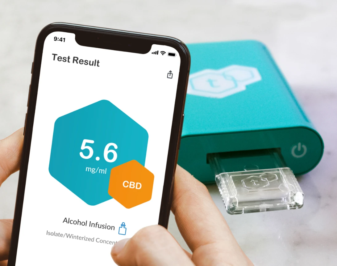 A turquoise t-check potency tester rests behind an iPhone which showcases the potency of the just tested strain inside of it.