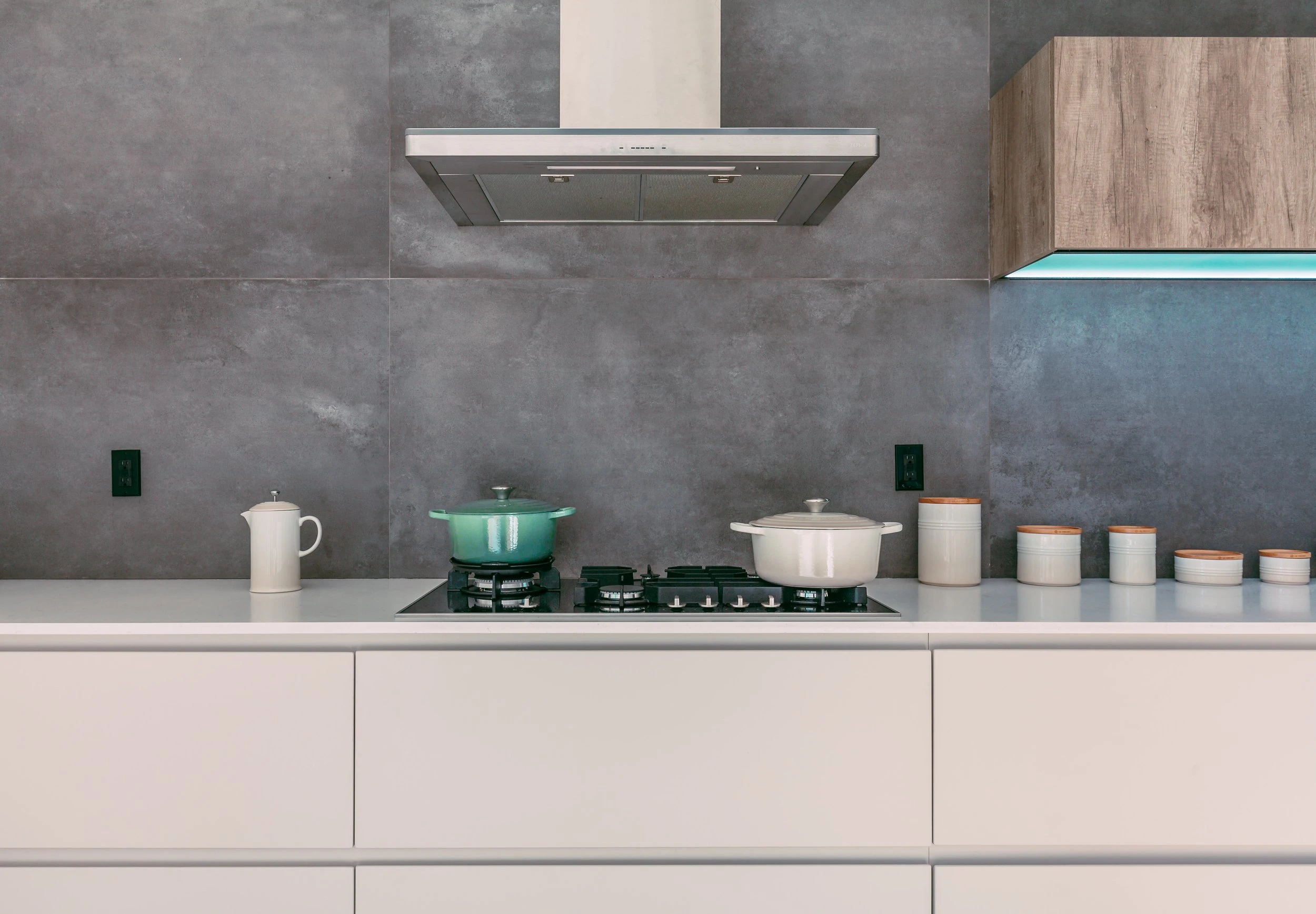 A white and turquoise pot sitting on a large kitchen stove with a white hood fan above it against a grey marble backsplash.