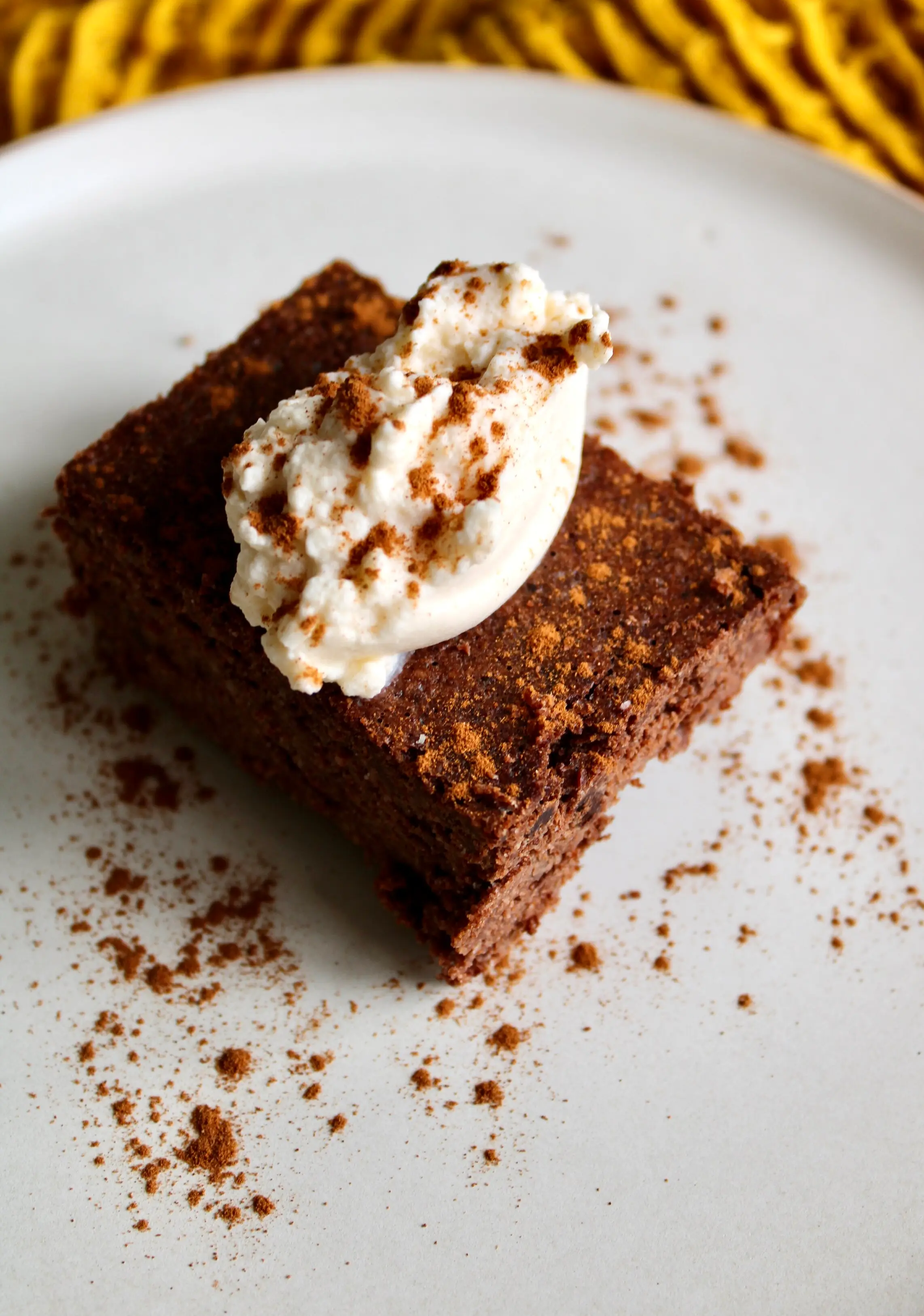 a cream plate with a square brownie resting on top of it, and its garnished with a scoop of ice cream.