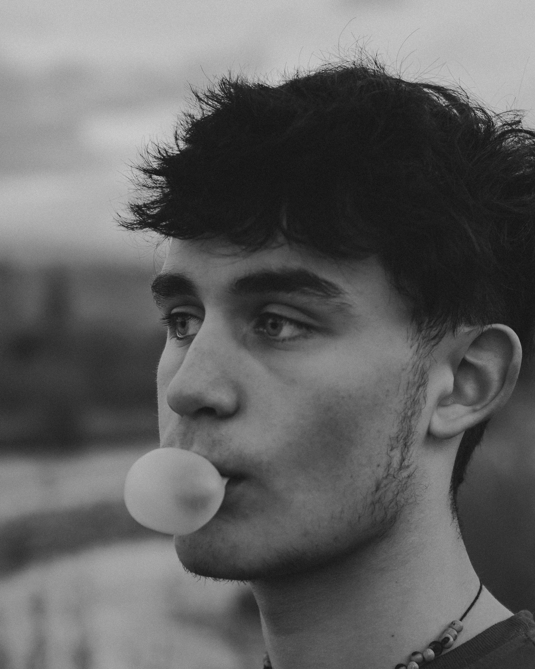 A man blowing a bubble with his gum with a black and white filter overlayed.