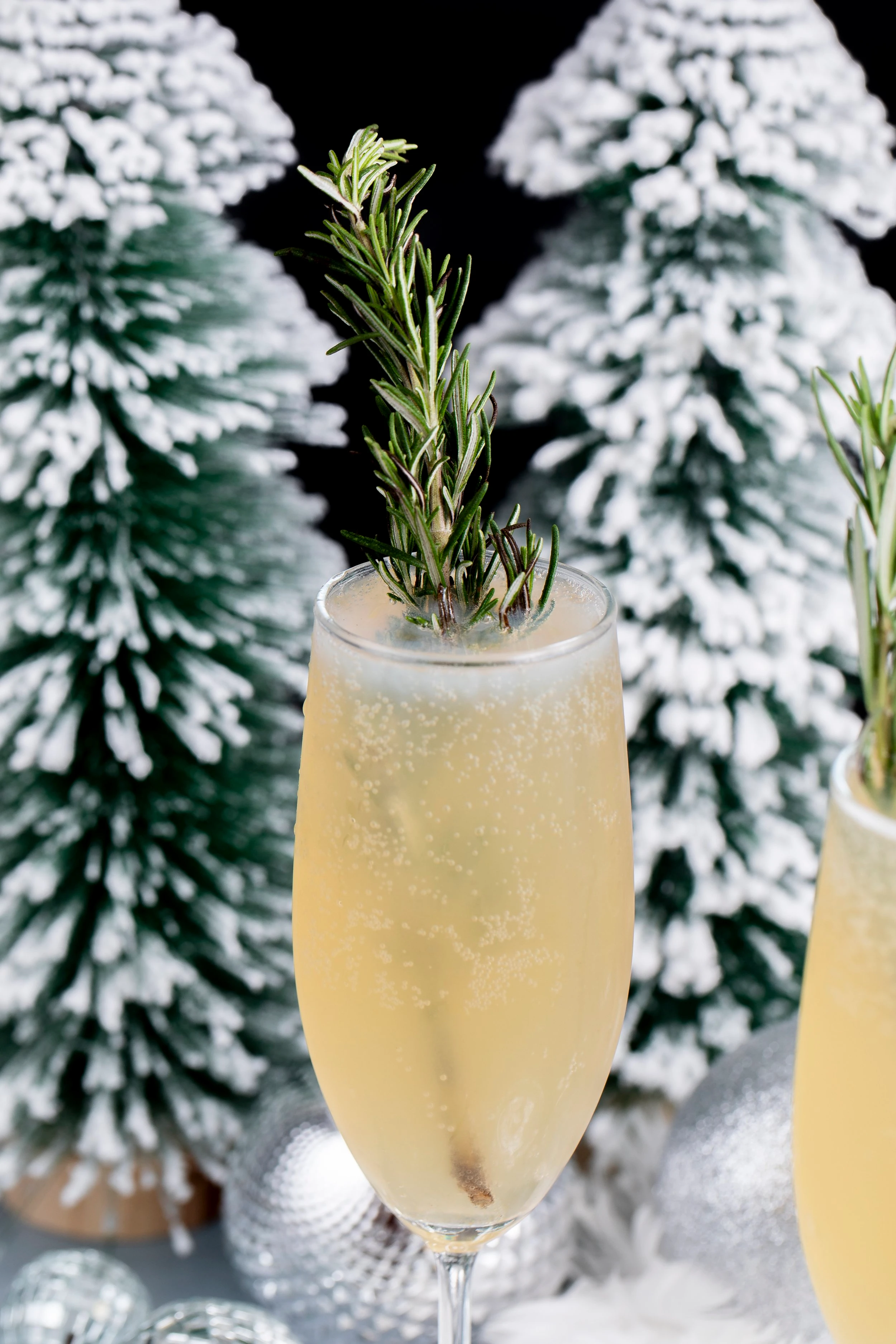 A champagne flute holding a cannabis infused new years spritz which features a large sprig of rosemary sticking out the top of the glass.