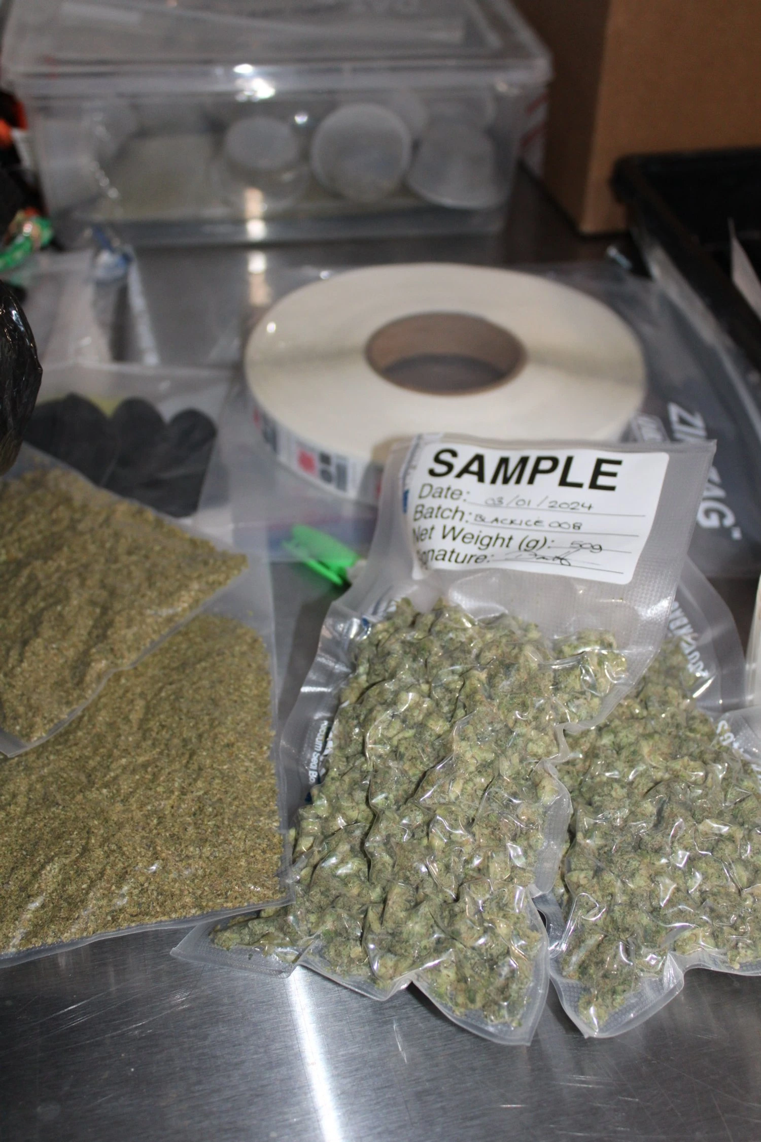 Some vacuumed sealed cannabis bags labeled "sample" sitting on a silver desk. 