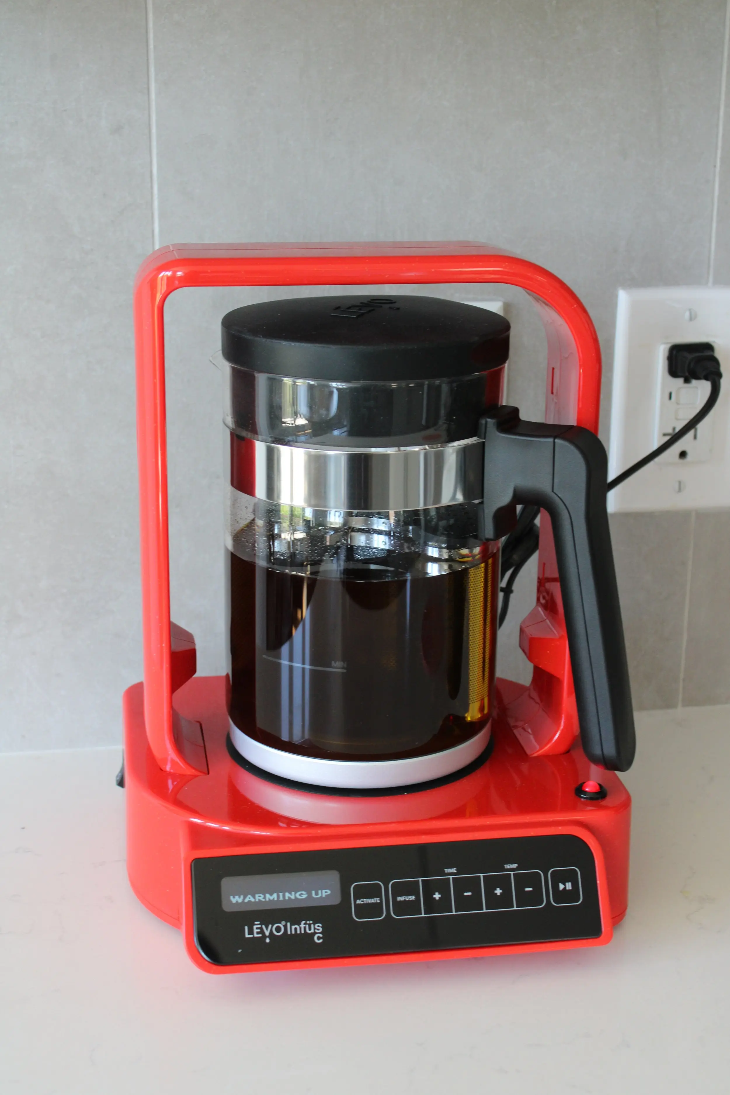 A red LEVO Infusion machine with the centre pot full of oil. The screen reads "warming up".