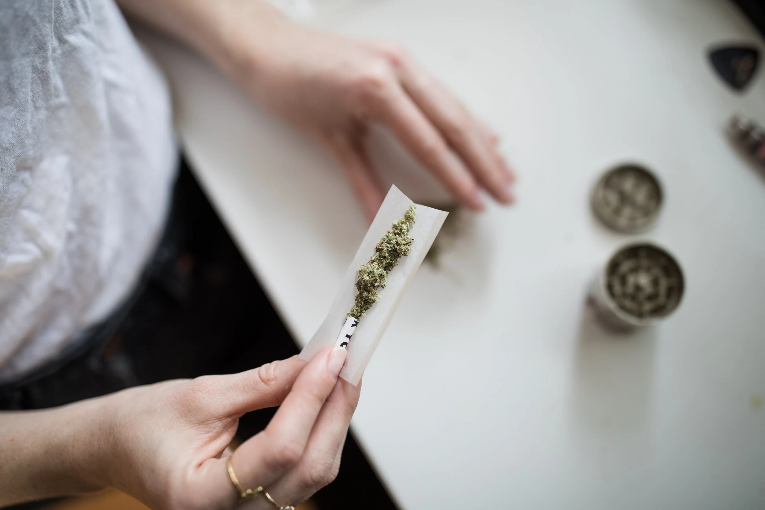 An aerial photograph of someone rolling a cannabis joint. The paper is open facing the camera which exposes the dried, ground cannabis.