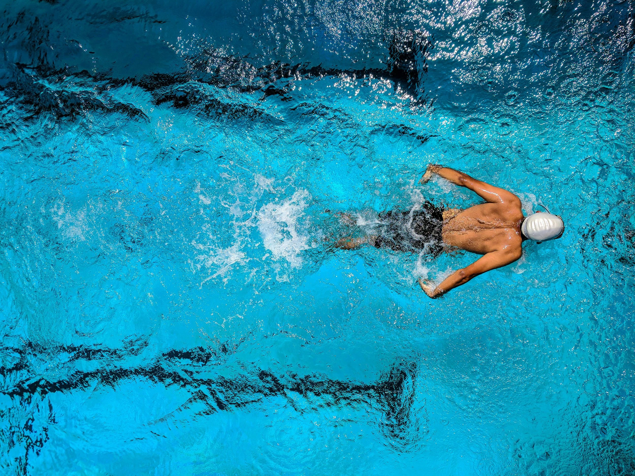 An aerial shot of a man swimming and doing the butterfly stroke with a grey swim cap on.