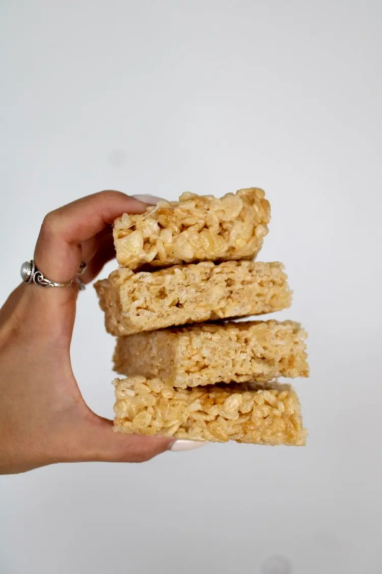 a hand holding a stack of 4 rice krispie squares against a white backdrop