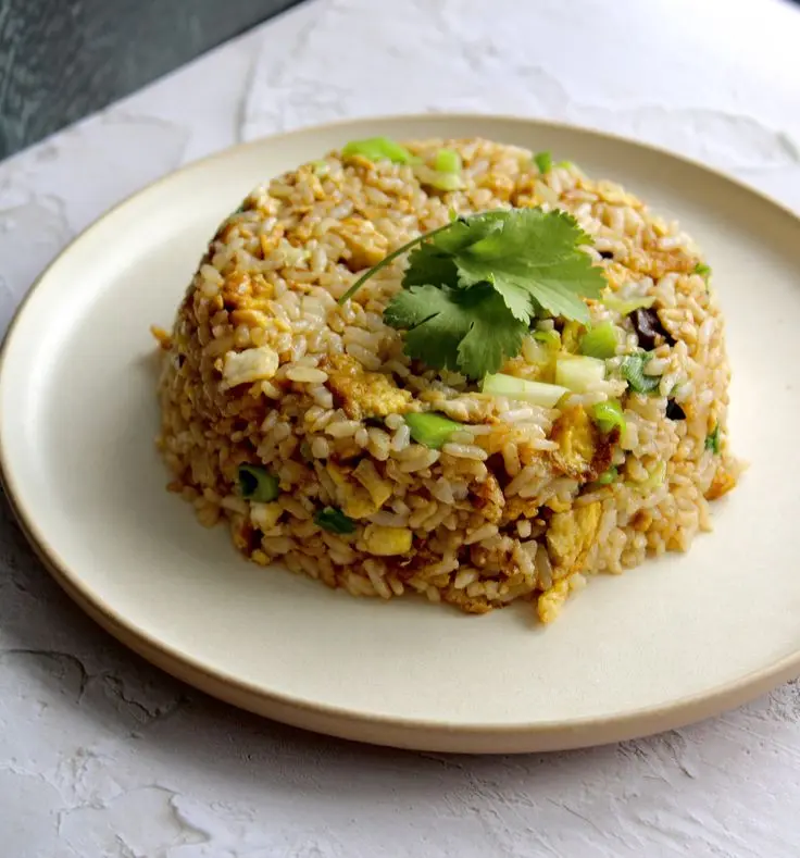 A cream coloured plate of a bed of infused fried rice with a few leaves of cilantro as a garnish on top.