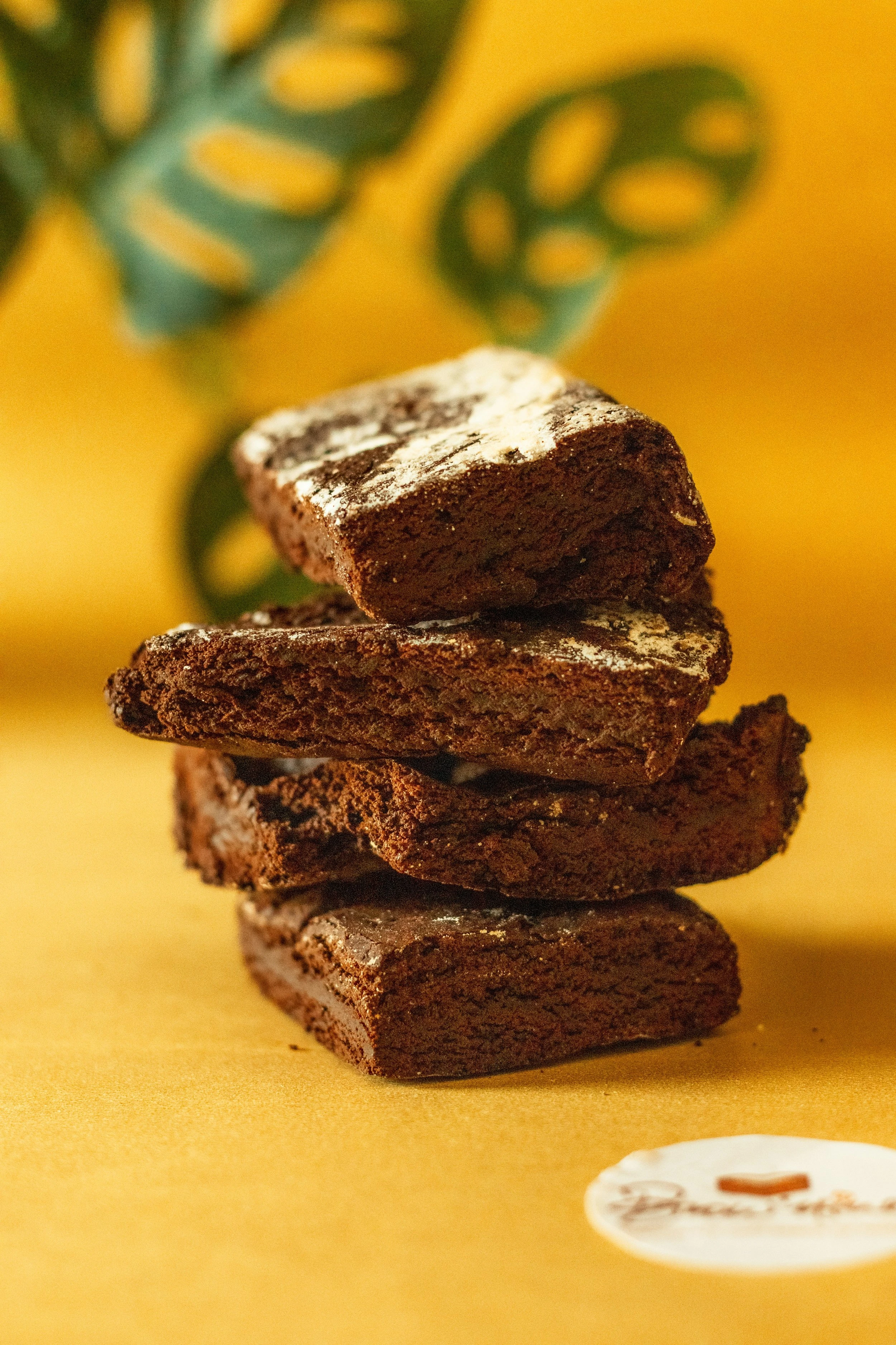 A stack of four chocolate brownies resting on top of each other on a yellow table.