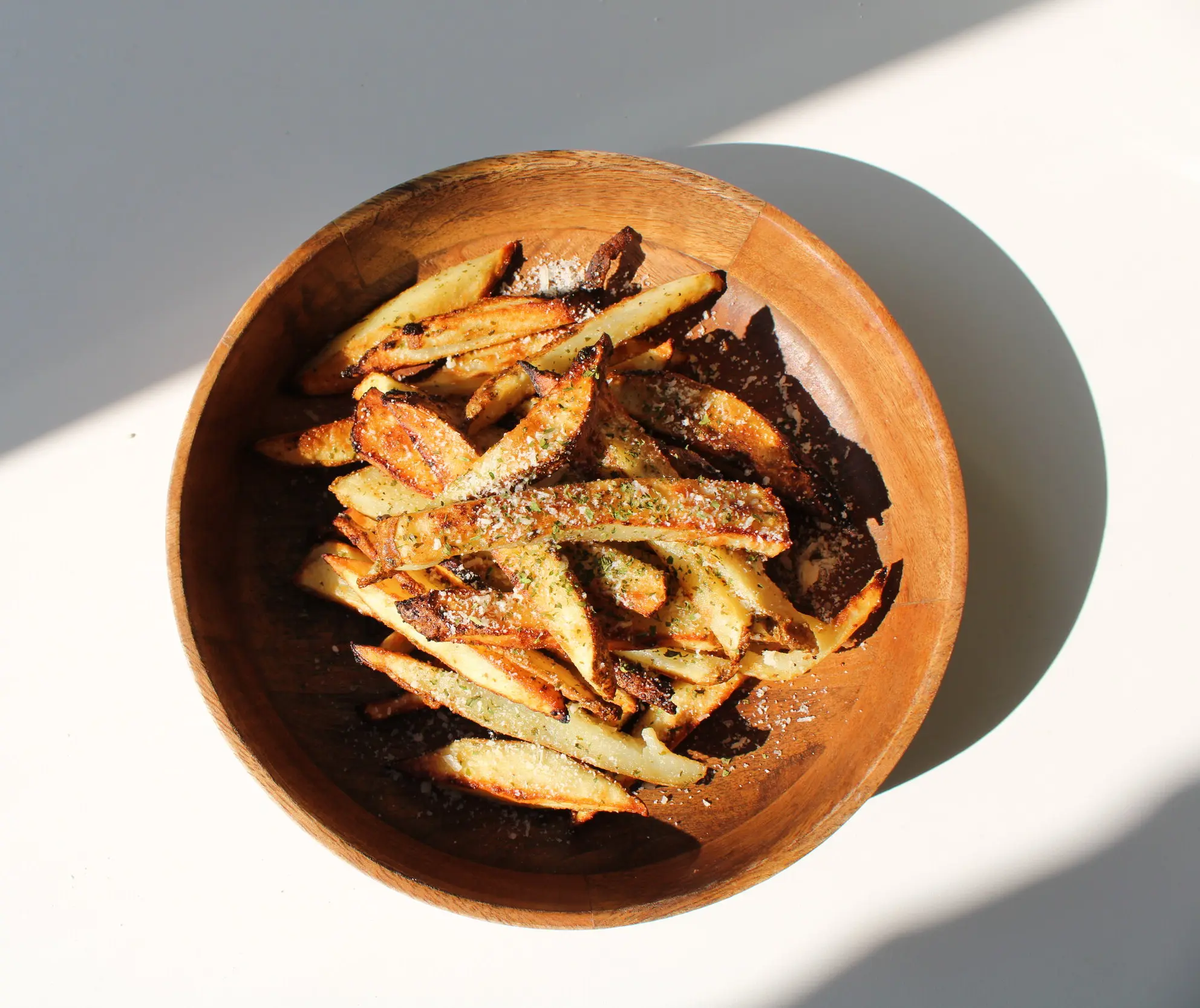 A wooden bowl of well seasoned French fries.