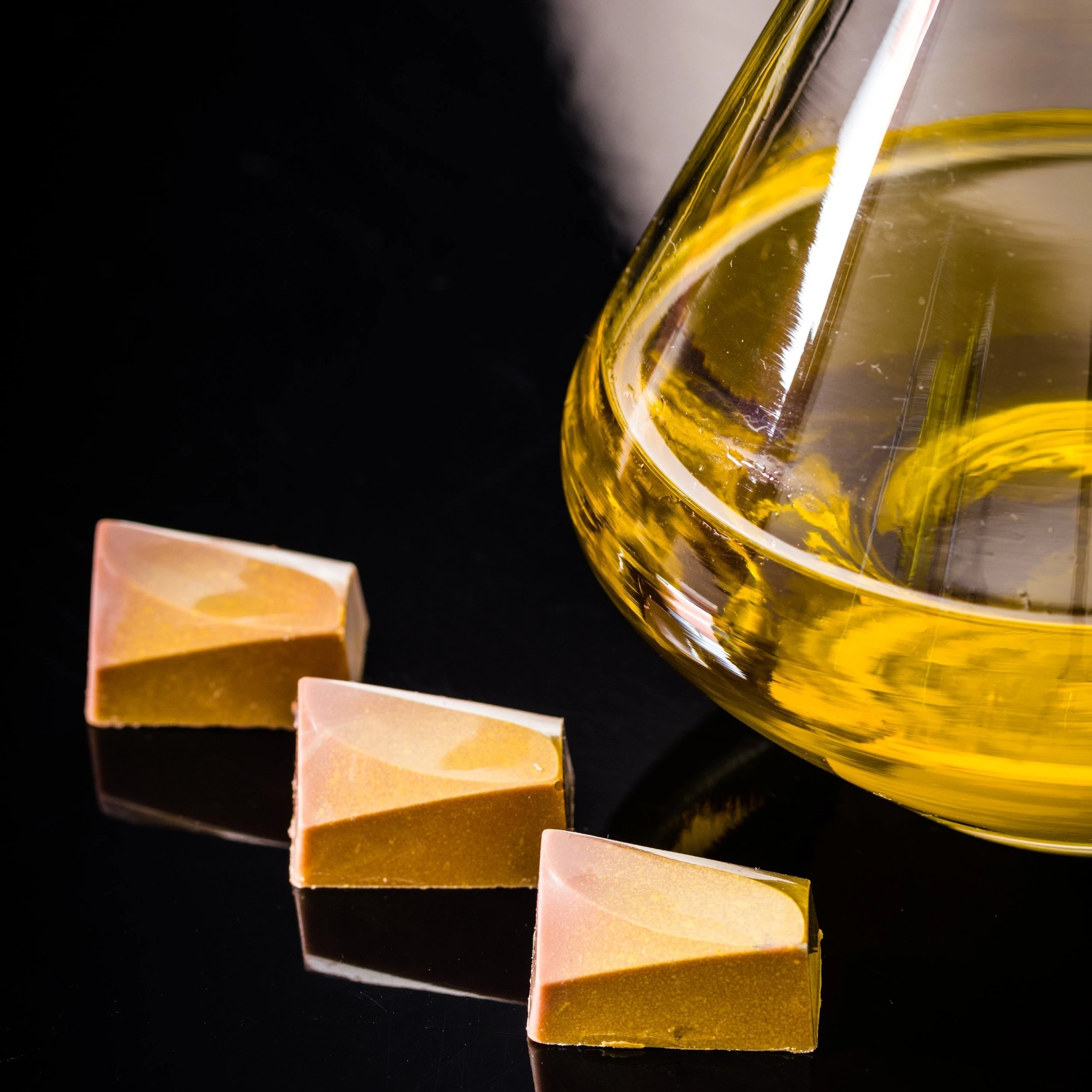 Three pieces of gold, pressed hash resting next to a glass liquid holder.