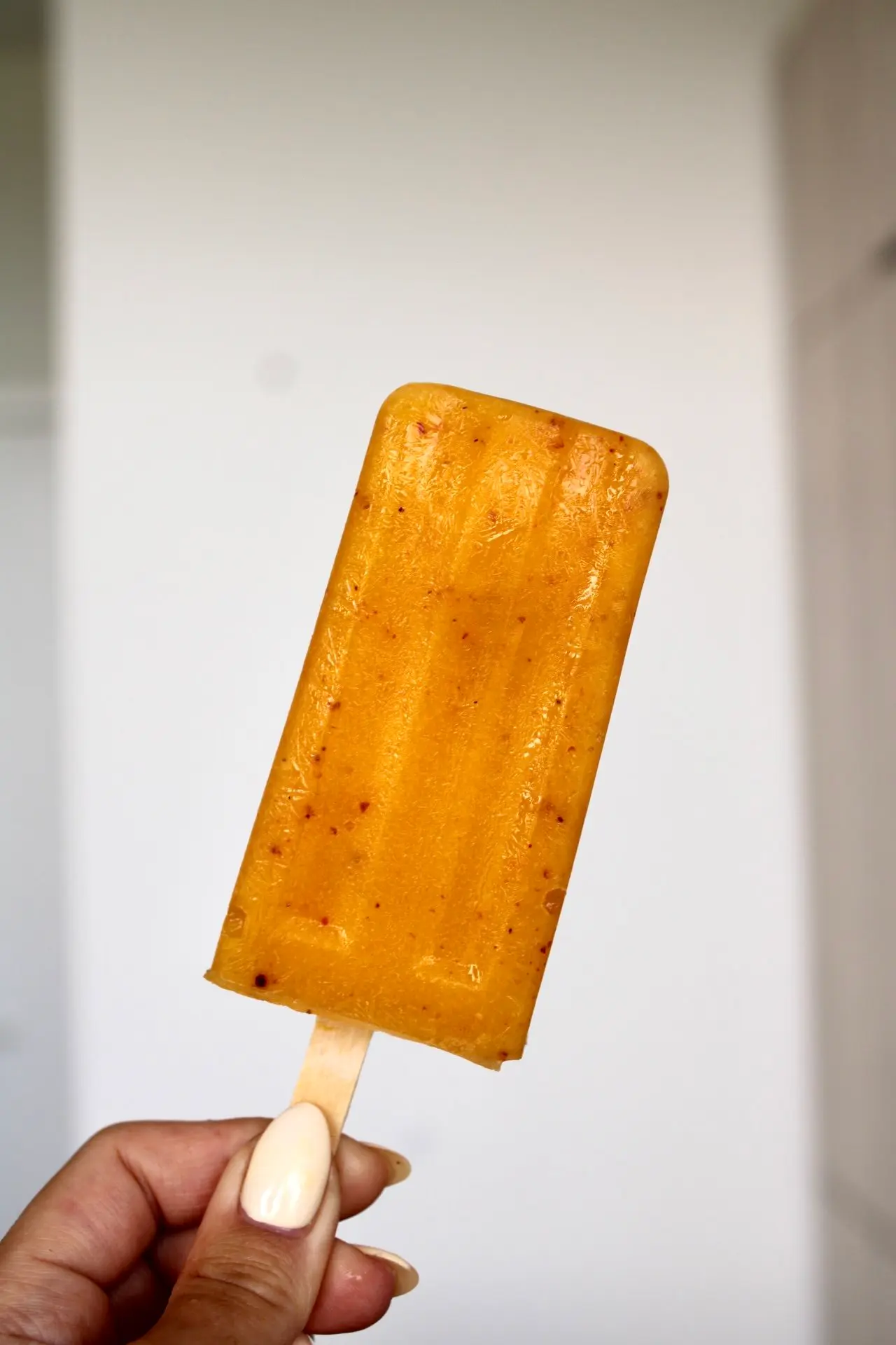 a hand holding up a mango coloured popsicle coated with tajin.