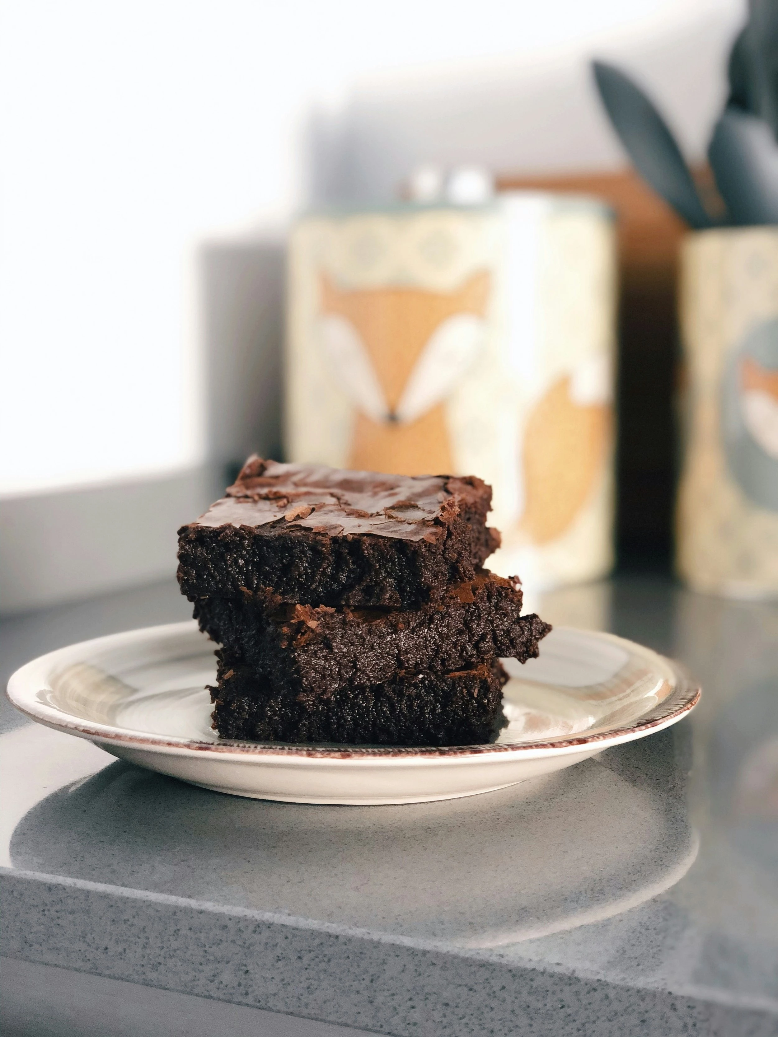 A stack of three ooey gooey chocolate brownies on a plate which rests on a marble counter.