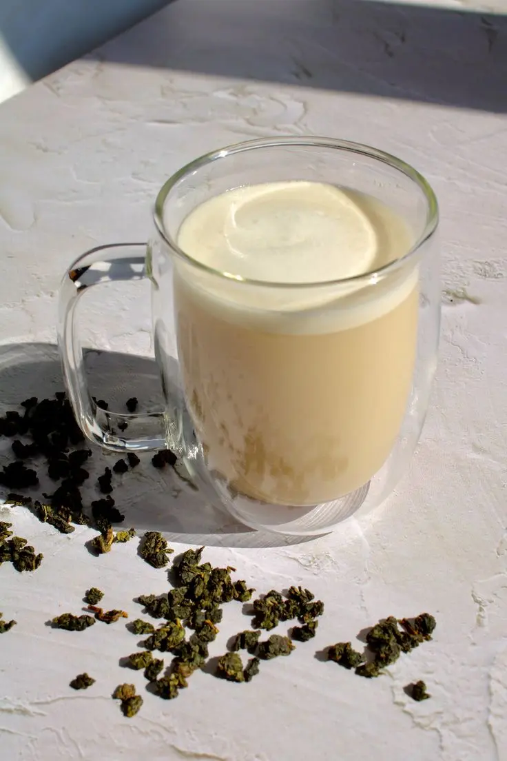 a clear glass mug with a yellow-ish hot beverage inside of it. There is a scattering of cannabis flower around its base. 