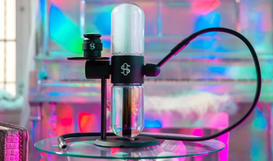 A black Studenglass gravity bong with vapour filling up the top chamber, against a neon pink, blue and green backdrop.