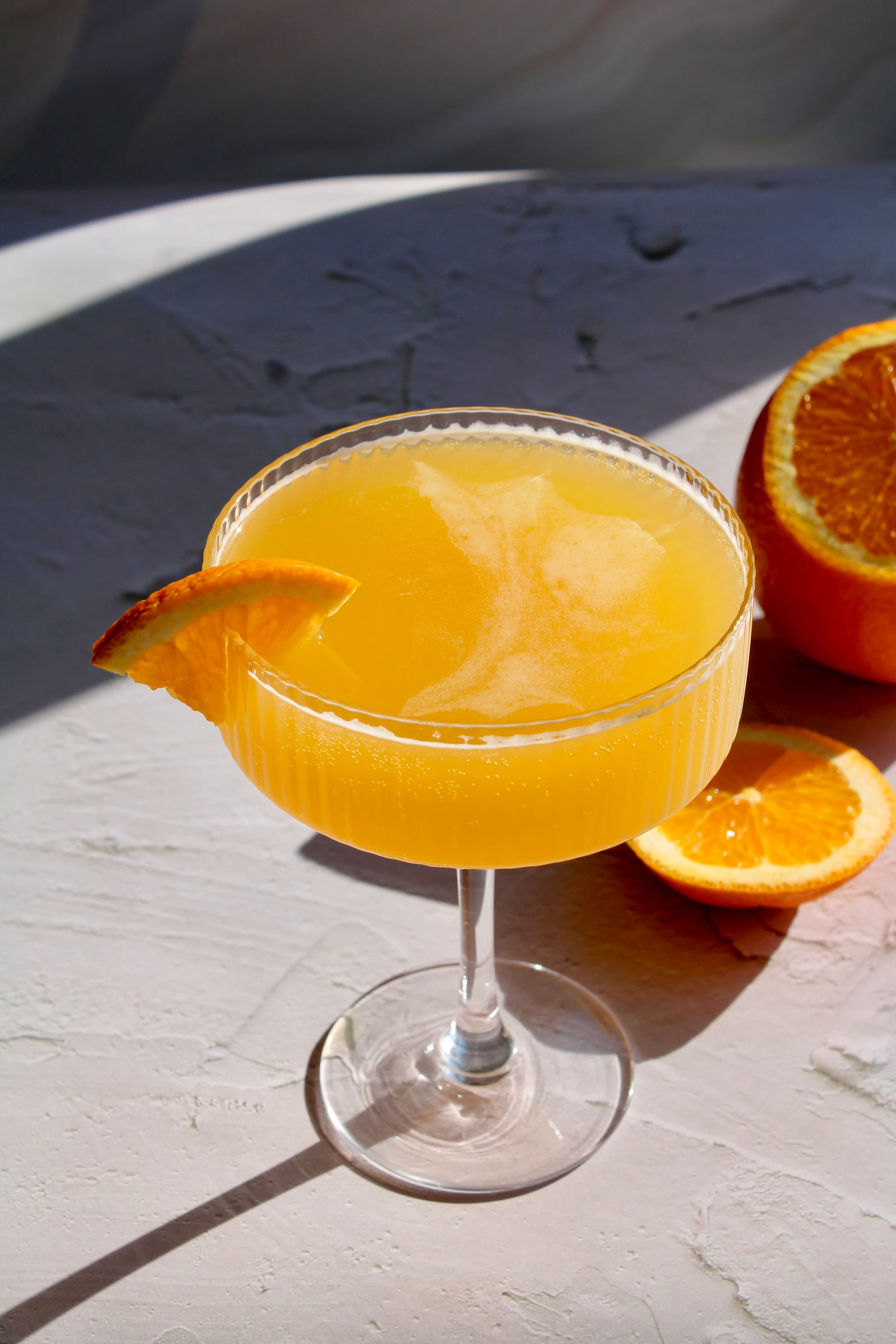 A martini glass full of a mimosa mocktail and garnished with a thinly quartered orange. 