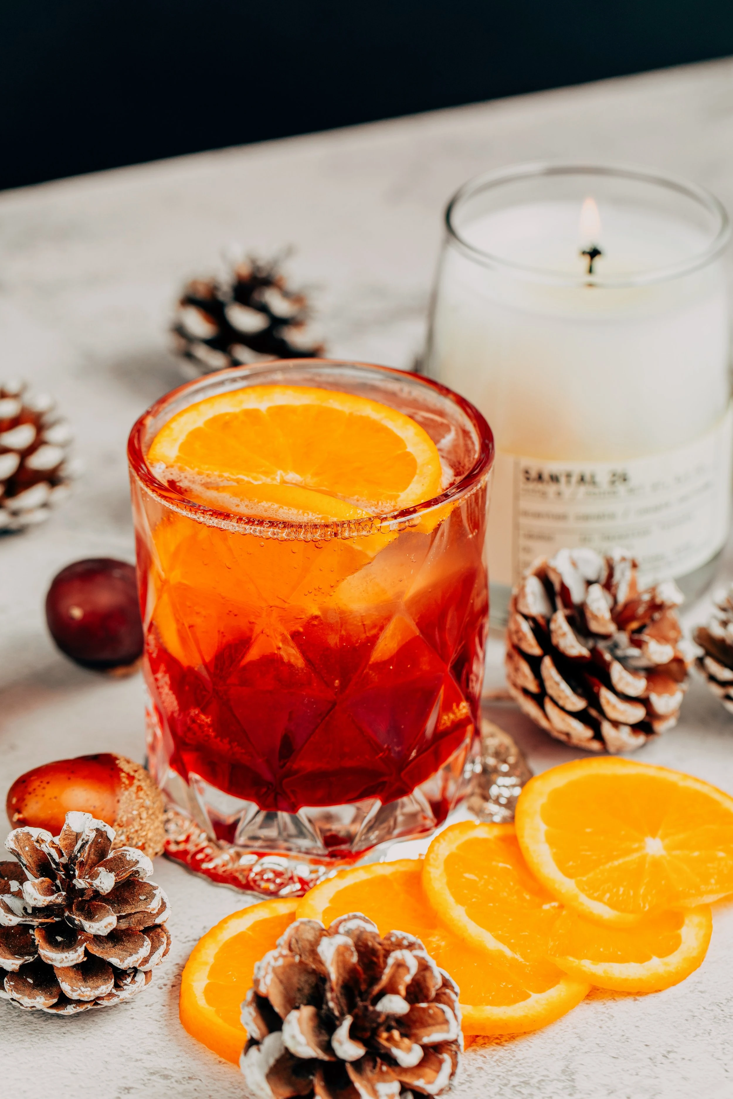 A red cannabis infused cranberry spritz sitting in a rocks glass and garnished with a slice of orange.