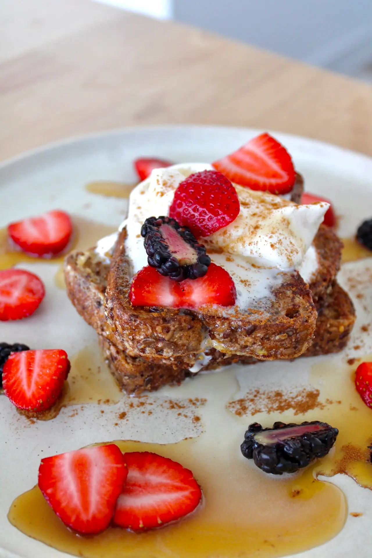 Two slices of French toast covered in sliced berries and topped with whipped cream and powdered cinnamon.