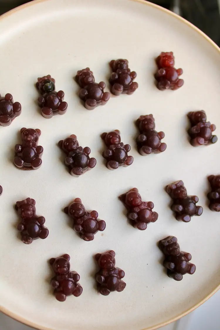 A cream coloured plate of burgundy coloured mini gummy bears in 4 loose rows.