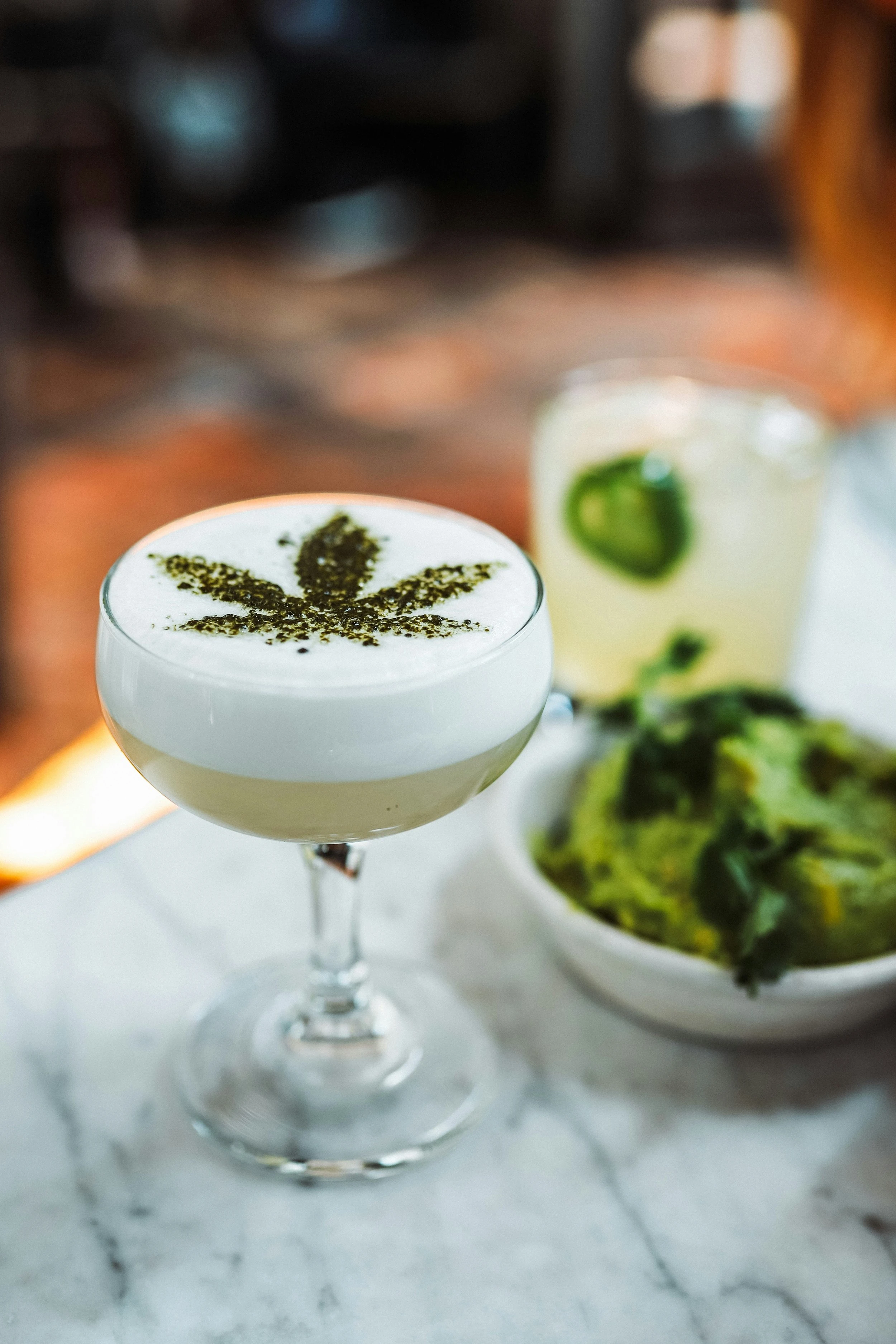 A martini glass full of an infused cocktail garnished with some powder in the shape of a cannabis leaf. 