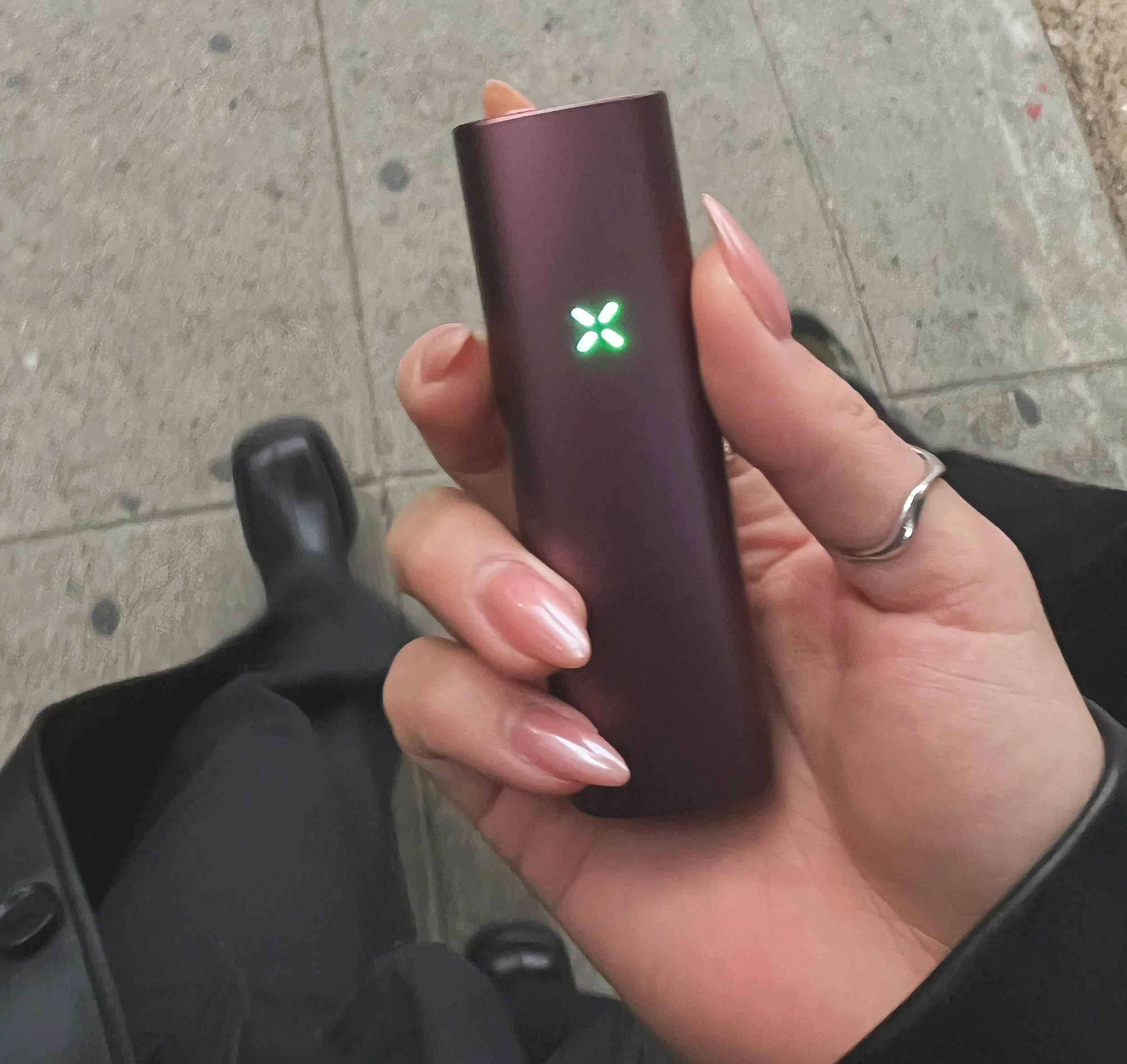 A hand with pink, long nails holding a PAX dried herb vaporizer. 