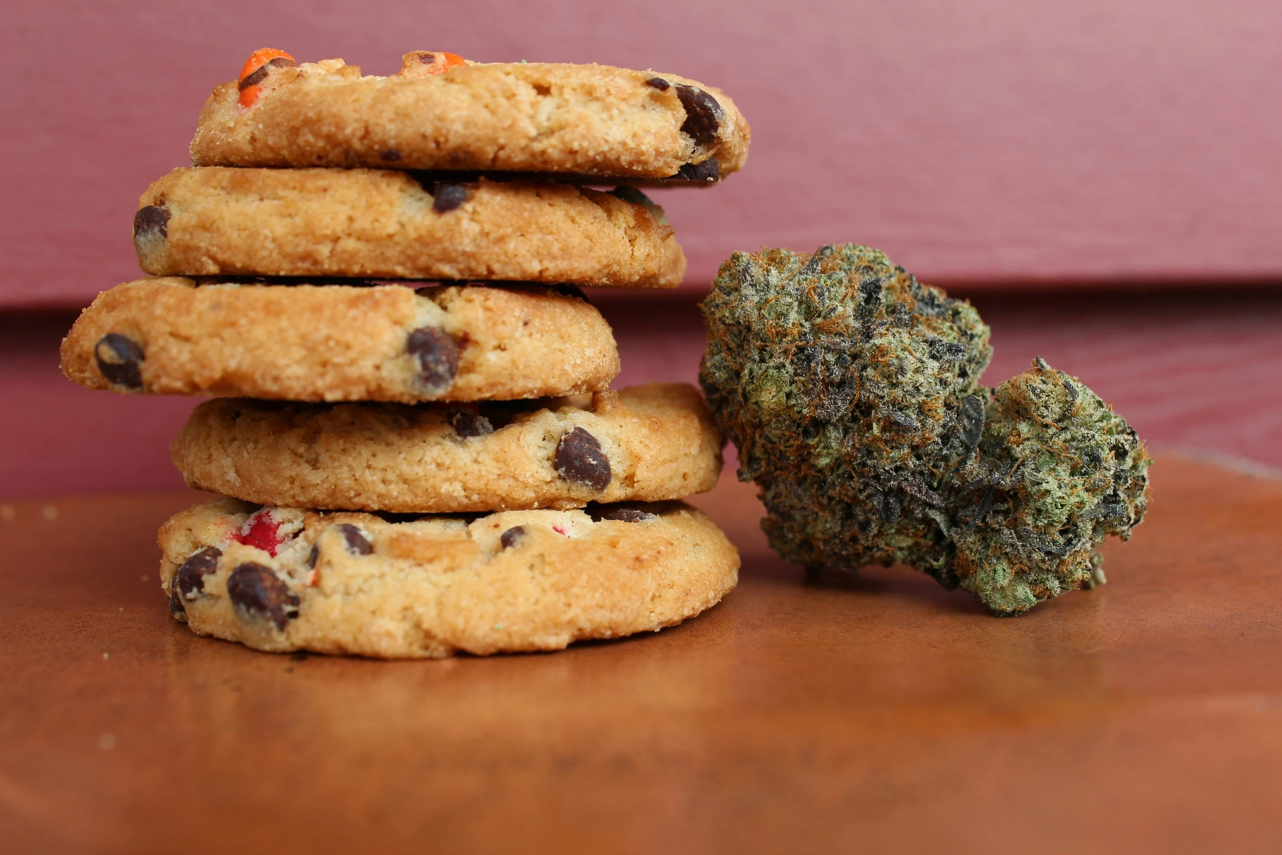 A stack of five Reese's pieces cookies resting next to a large cannabis bud. 