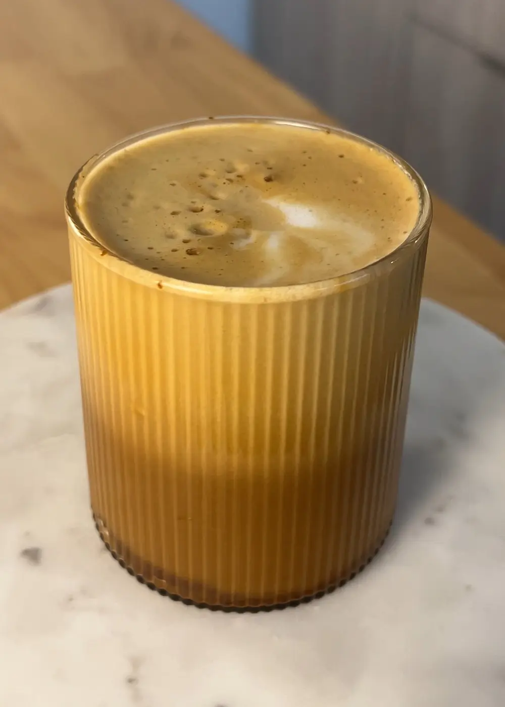 A glass mug with a beautiful looking latte full to the brim in it.