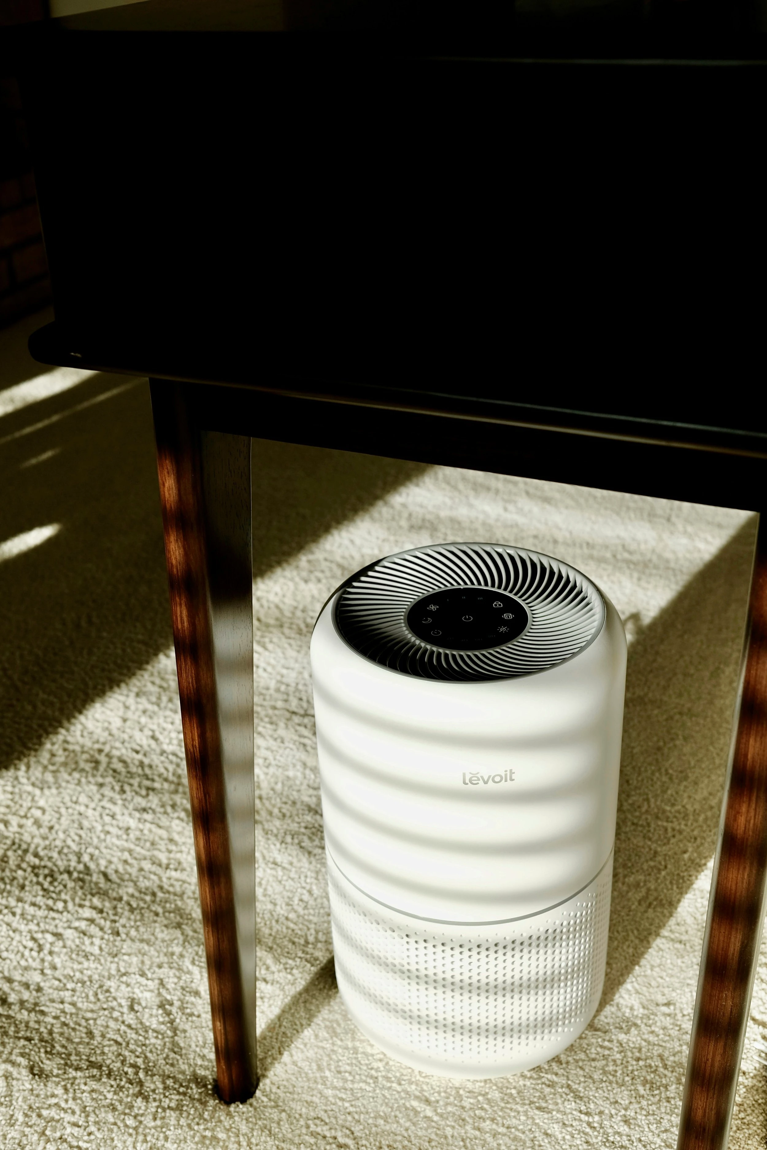 A white air purifier resting on a white carpeted living room floor. 