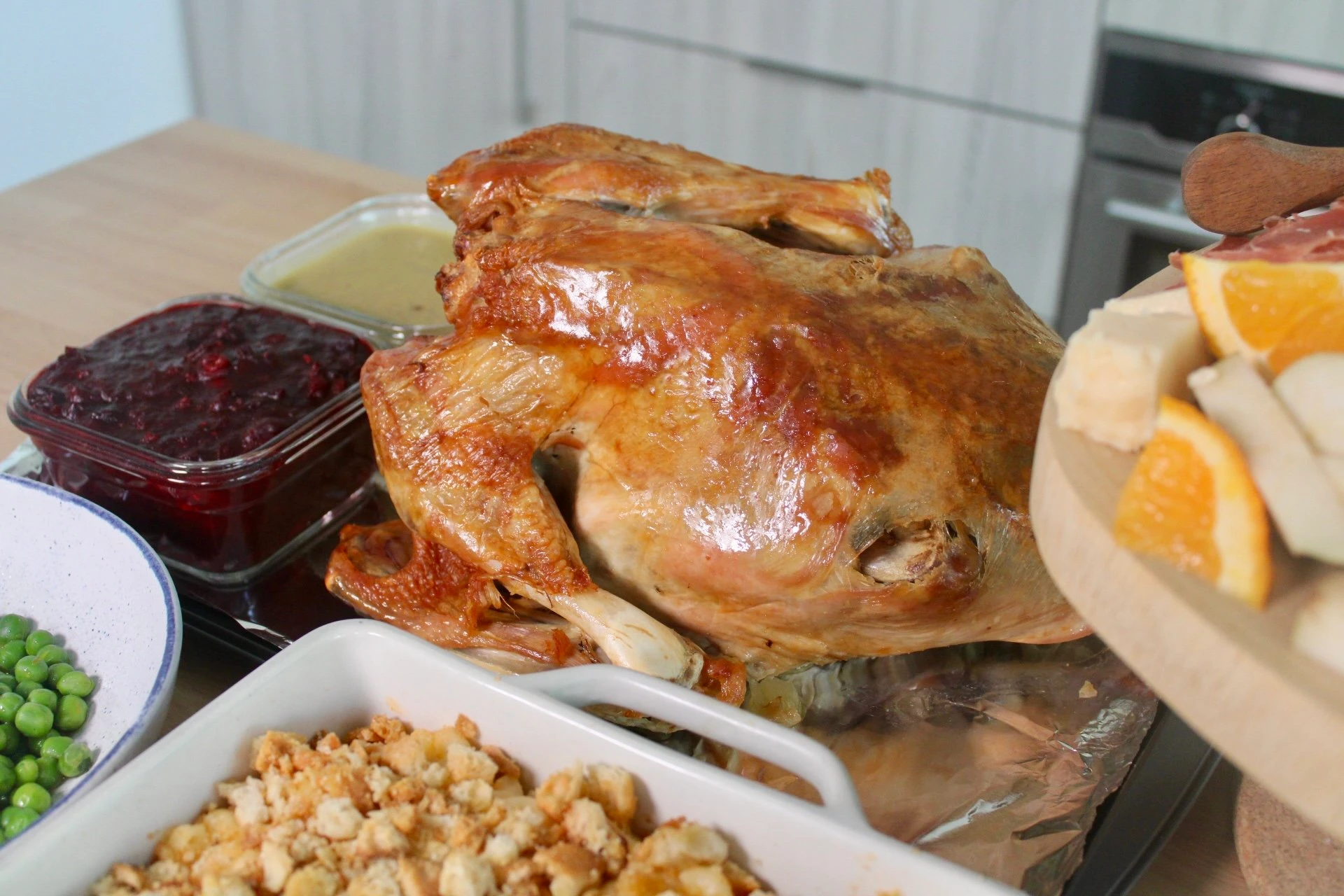 A roasted turkey surrounded by all of the thanksgiving fixings including stuffing, cranberry sauce and peas.