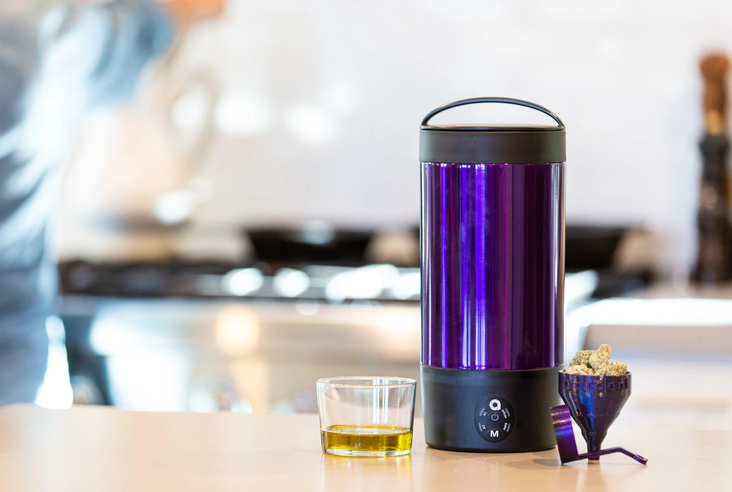 The ARDENT Mini infusion device in the colour purple rests on a counter with a jar 1/3 of the way full of infused oil next to it.