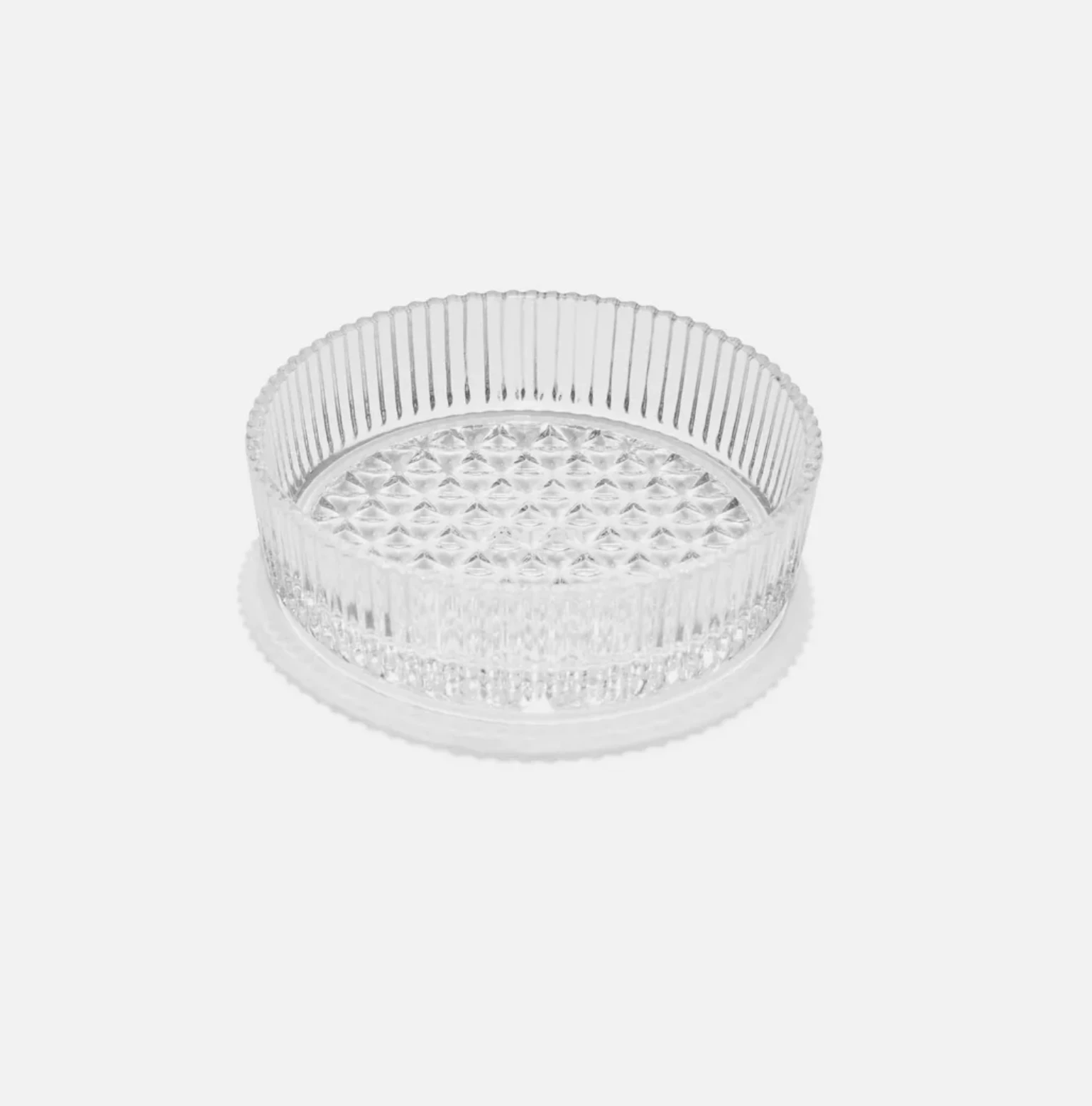 A clear glass ashtray which mimics crystal sits on an all white surface. 