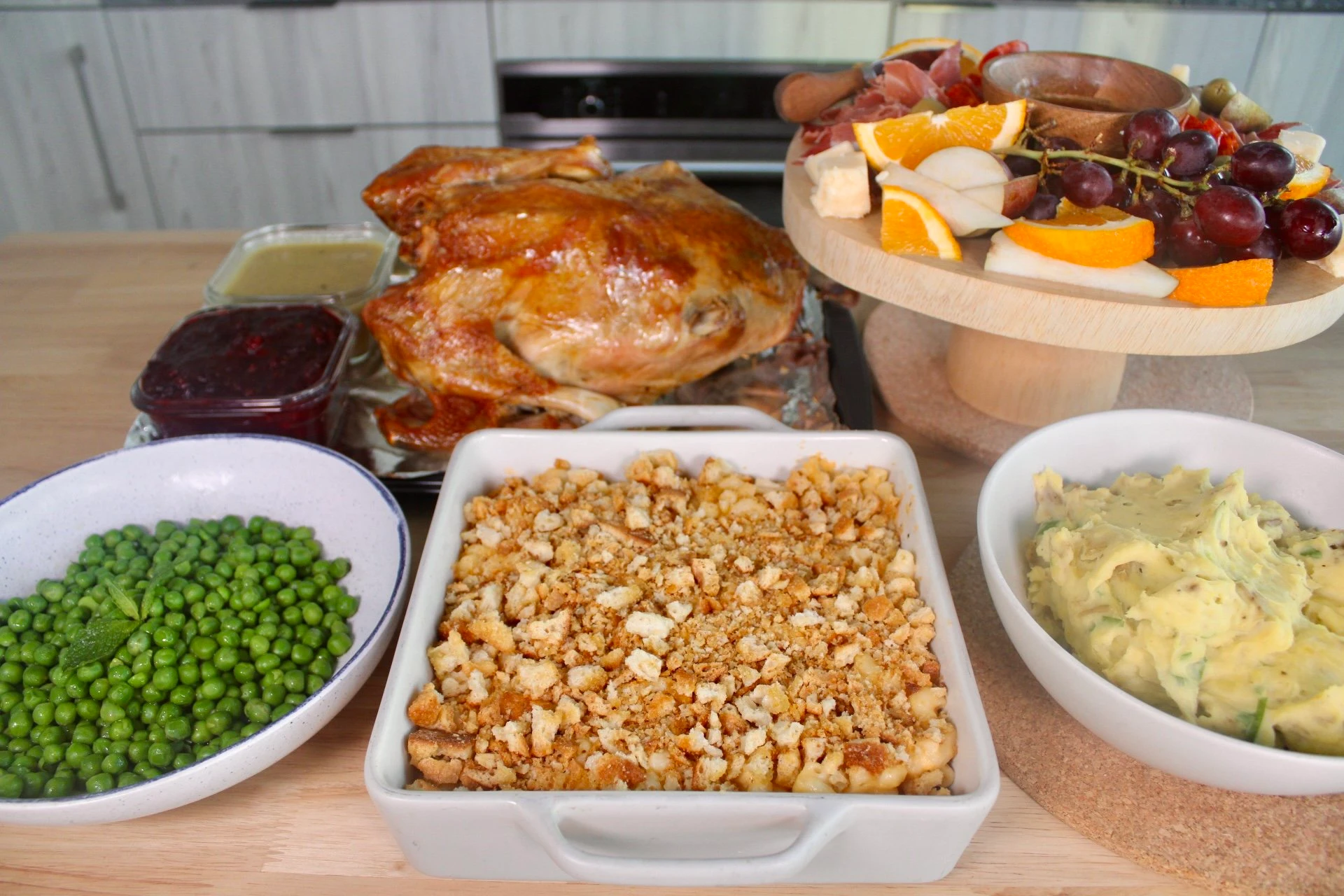 a counter full of square and circular cooking dishes all full of different thanksgiving meal staples including a turkey, peas, stuffing and mashed potatoes. 