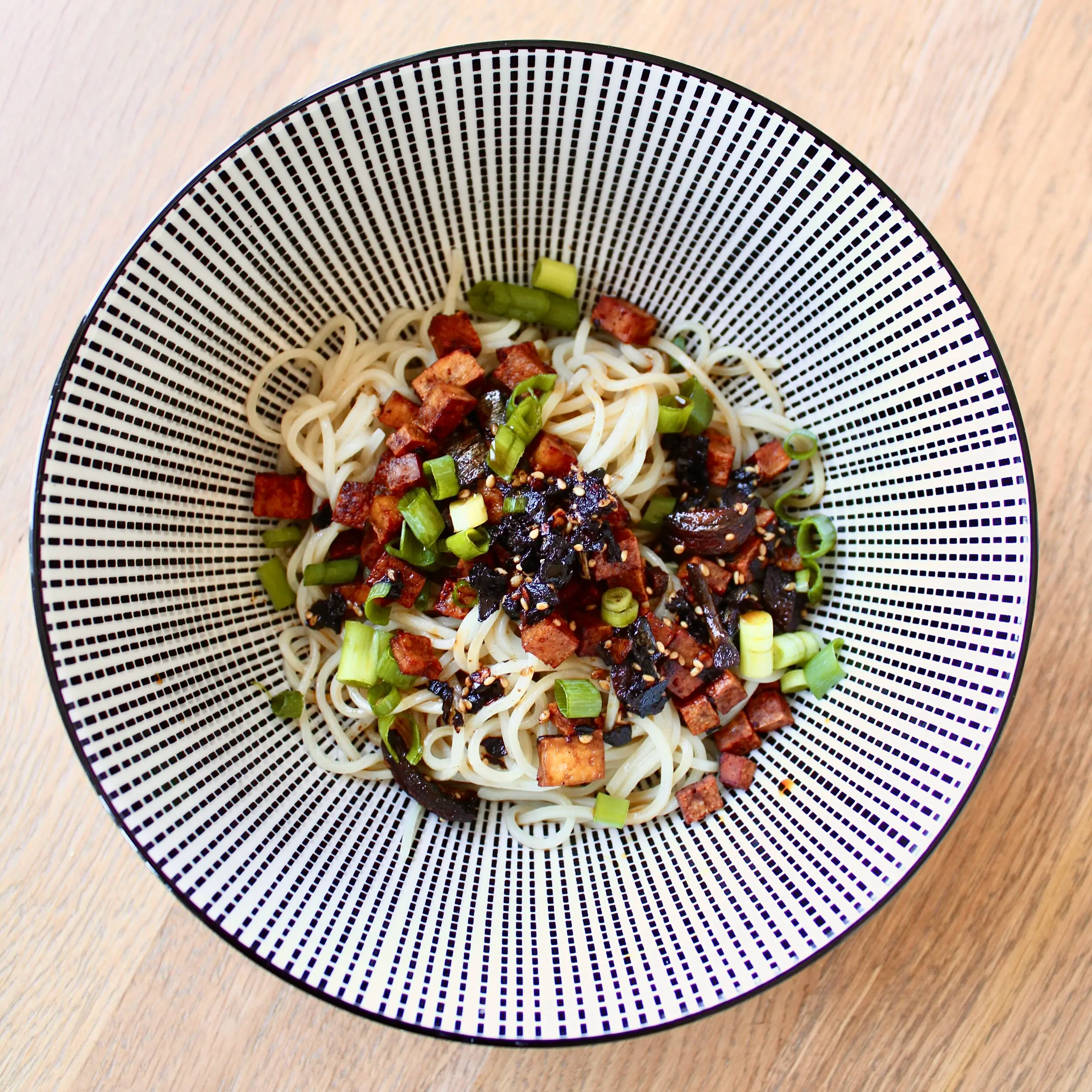 A blue and white striped bowl full of ramen noodles. The top features green onions and chili oil.