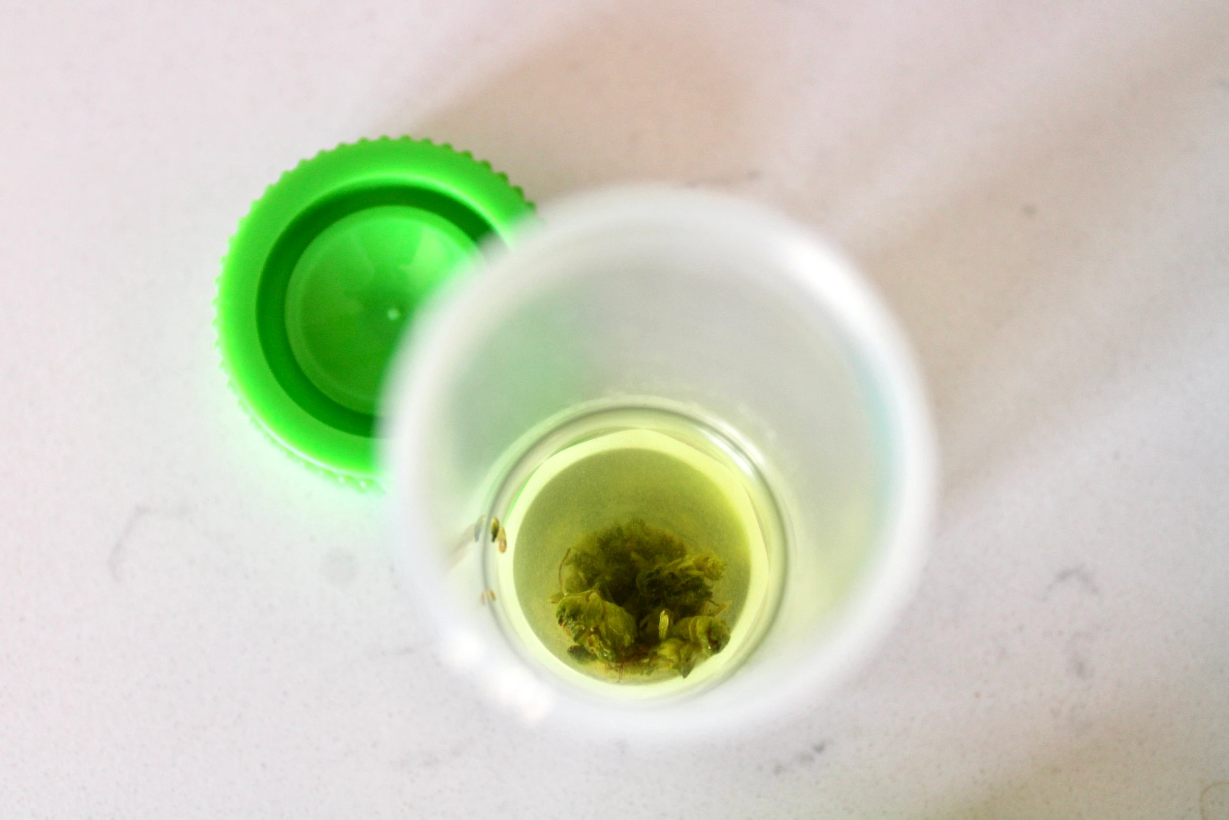 A clear tube, open, with a cannabis bud and solution inside of it, as the cap rests beside it on a marble countertop.