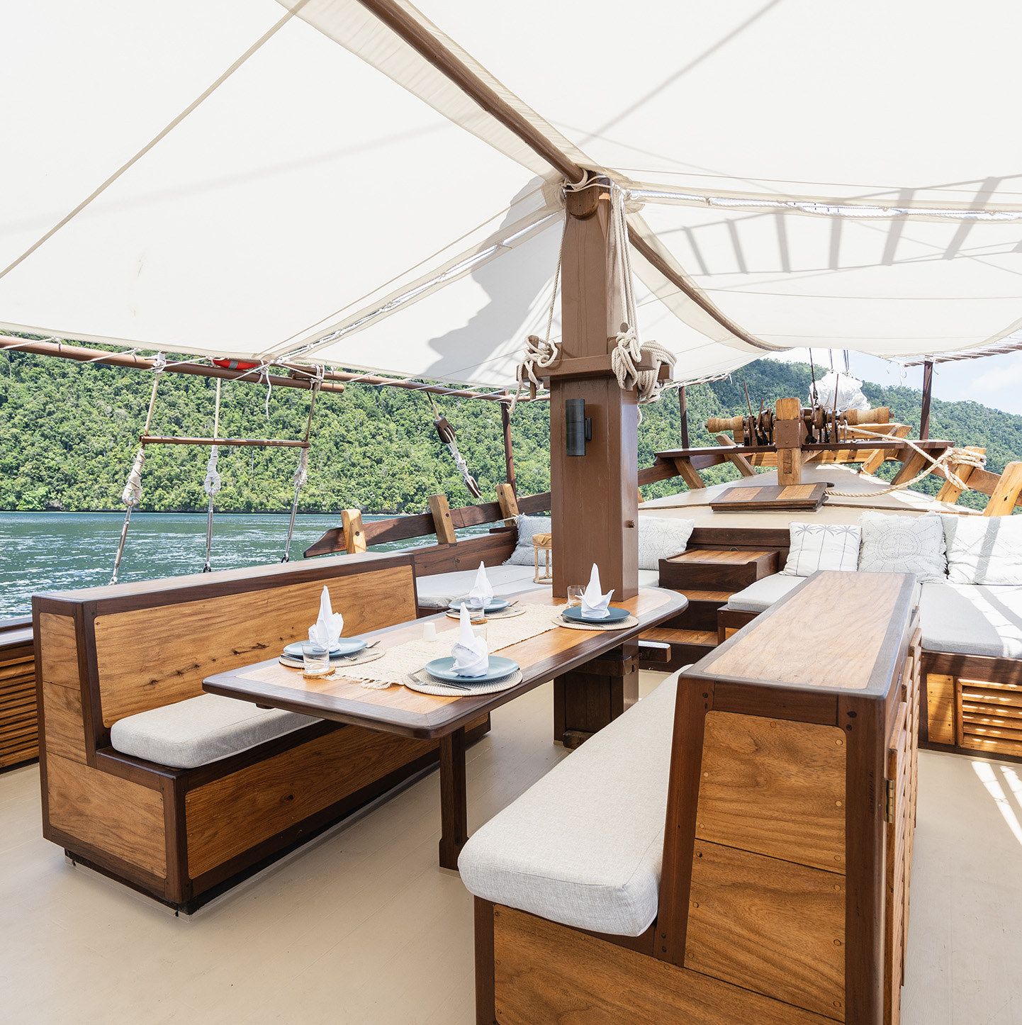 The foredeck on Dewata beneath the white awning with a table and cushioned benches.